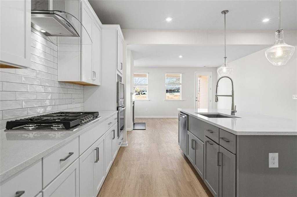 Modern open-concept kitchen with white shaker cabinets, subway tile backsplash, quartz island, and gas cooktop in The Glenwood C at Wehunt Meadows, Hoschton, GA