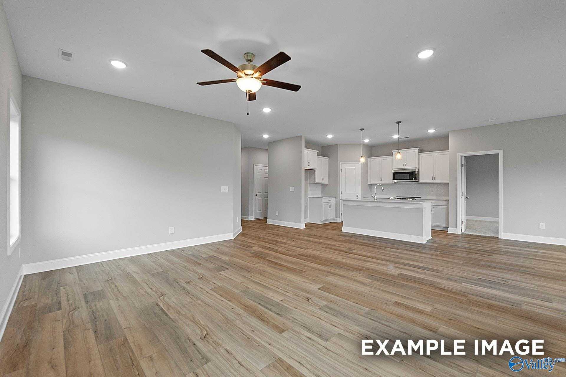 Open-concept living kitchen with hardwood floors, white cabinets, island, and ceiling fan in Davidson Homes The Franklin E, Hazel Green, Alabama