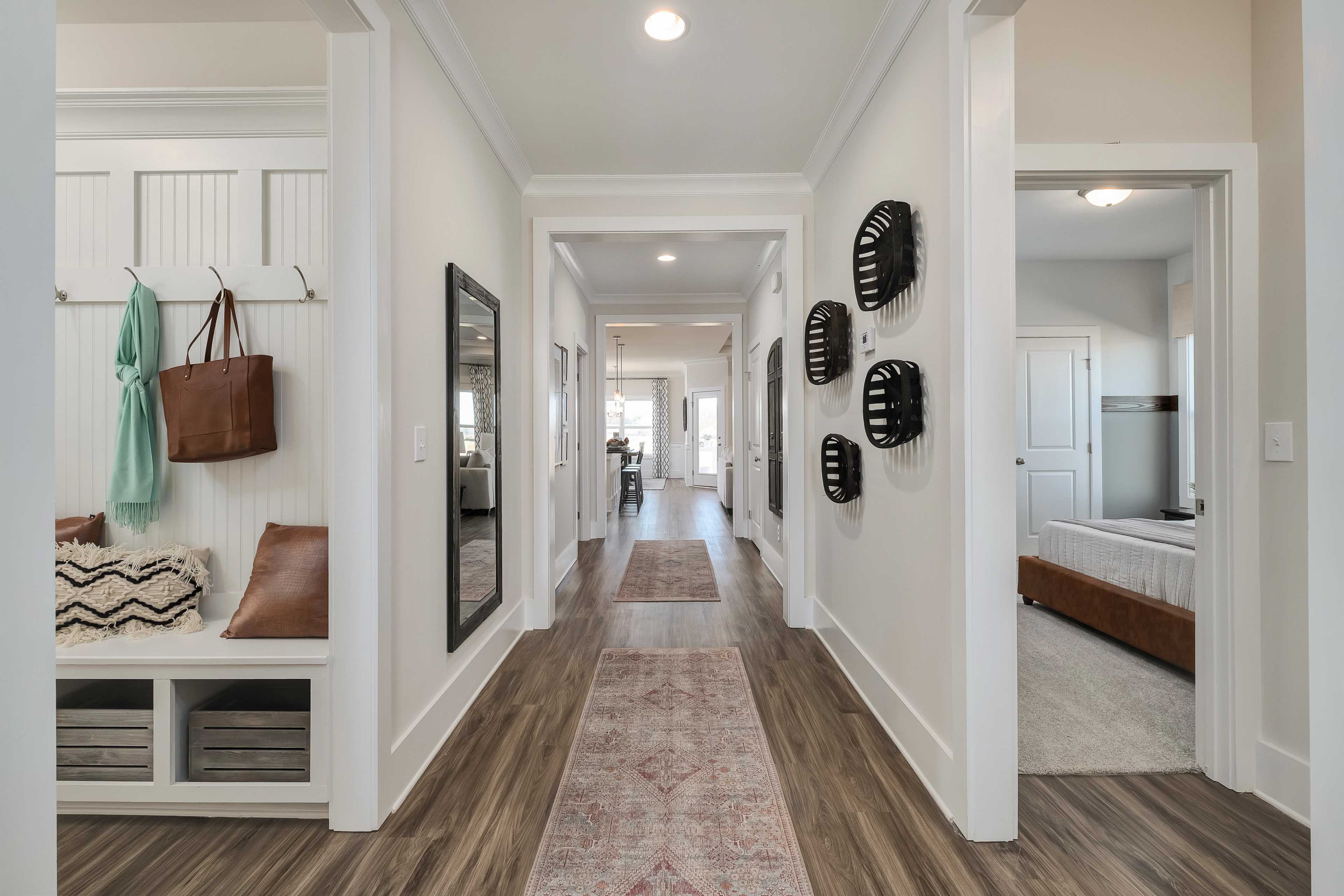 Spacious hallway with hardwood floors and Persian runner rug at Mallard Landing in Athens Alabama featuring entry bench, hooks, and wall art