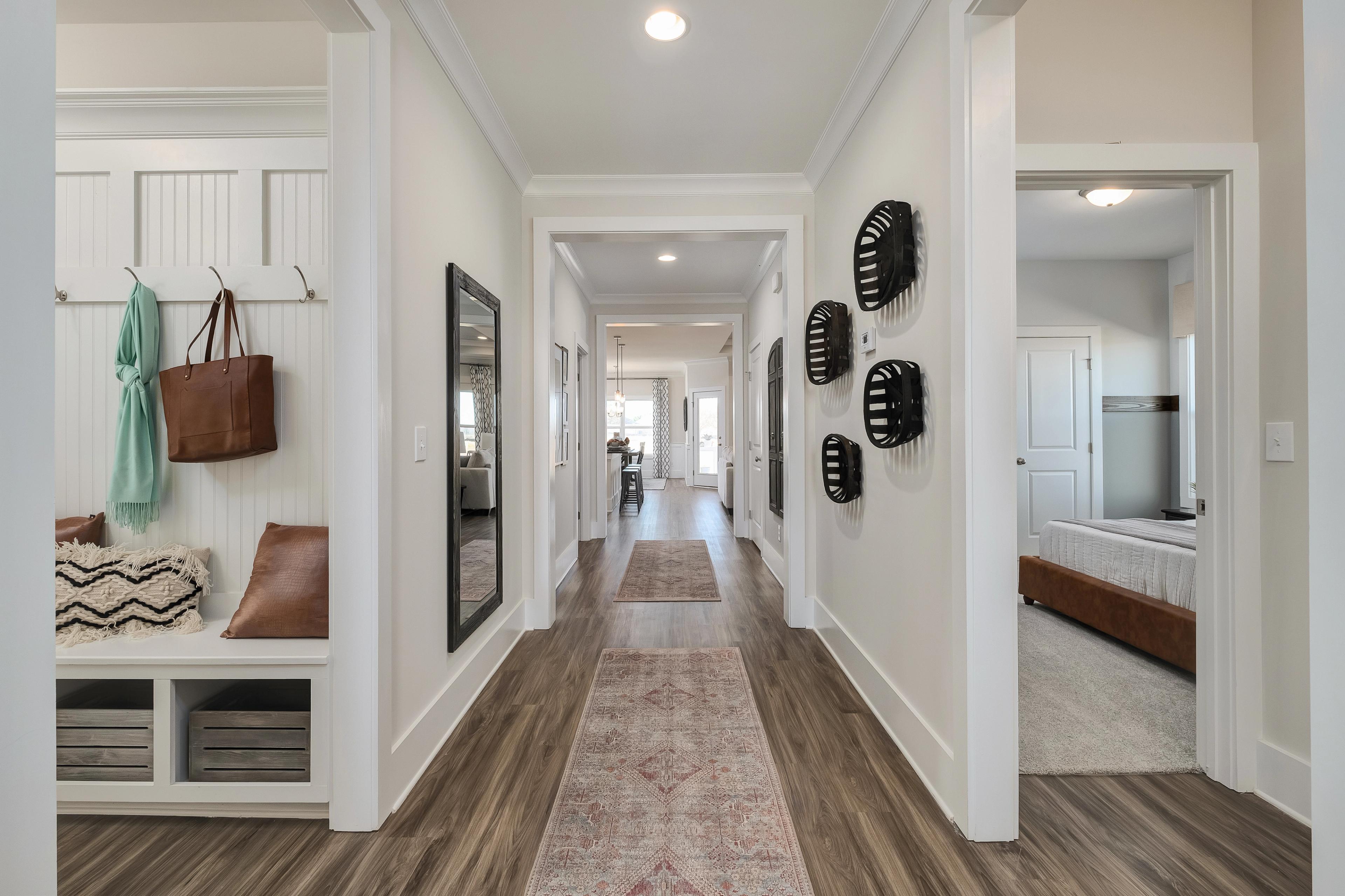 Spacious hallway with hardwood floors and Persian runner rug at Mallard Landing in Athens Alabama featuring entry bench, hooks, and wall art