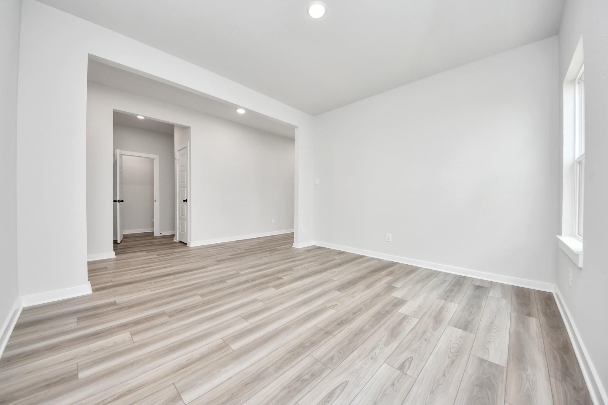 Bright, open-concept bedroom with light wood-style flooring in The Sorrento E floor plan at Sundance Cove, Crosby, Texas.