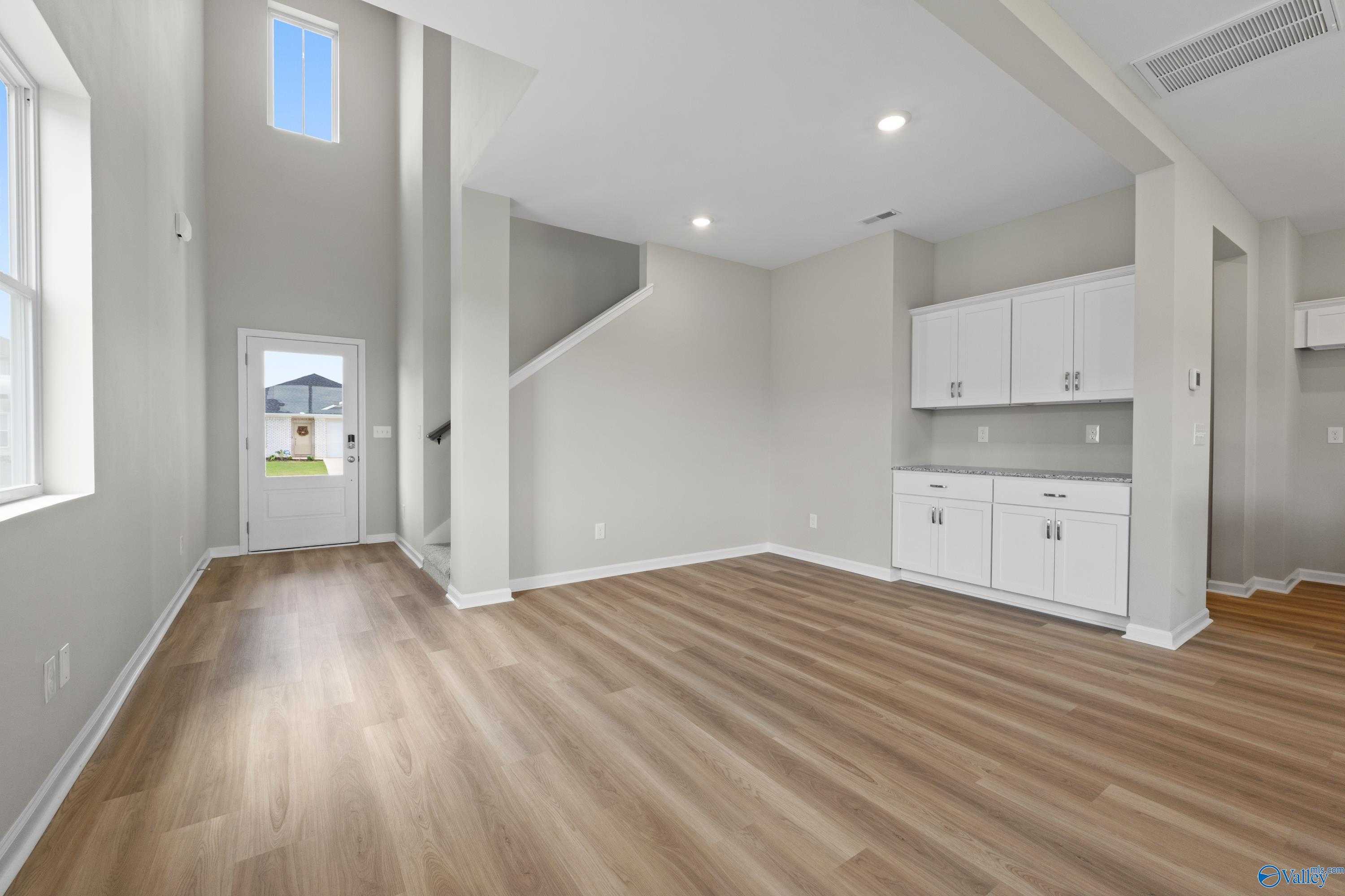 Bright entry foyer with high ceilings, hardwood floors, open staircase, and white kitchen cabinets in The Augusta home, Madison, Alabama