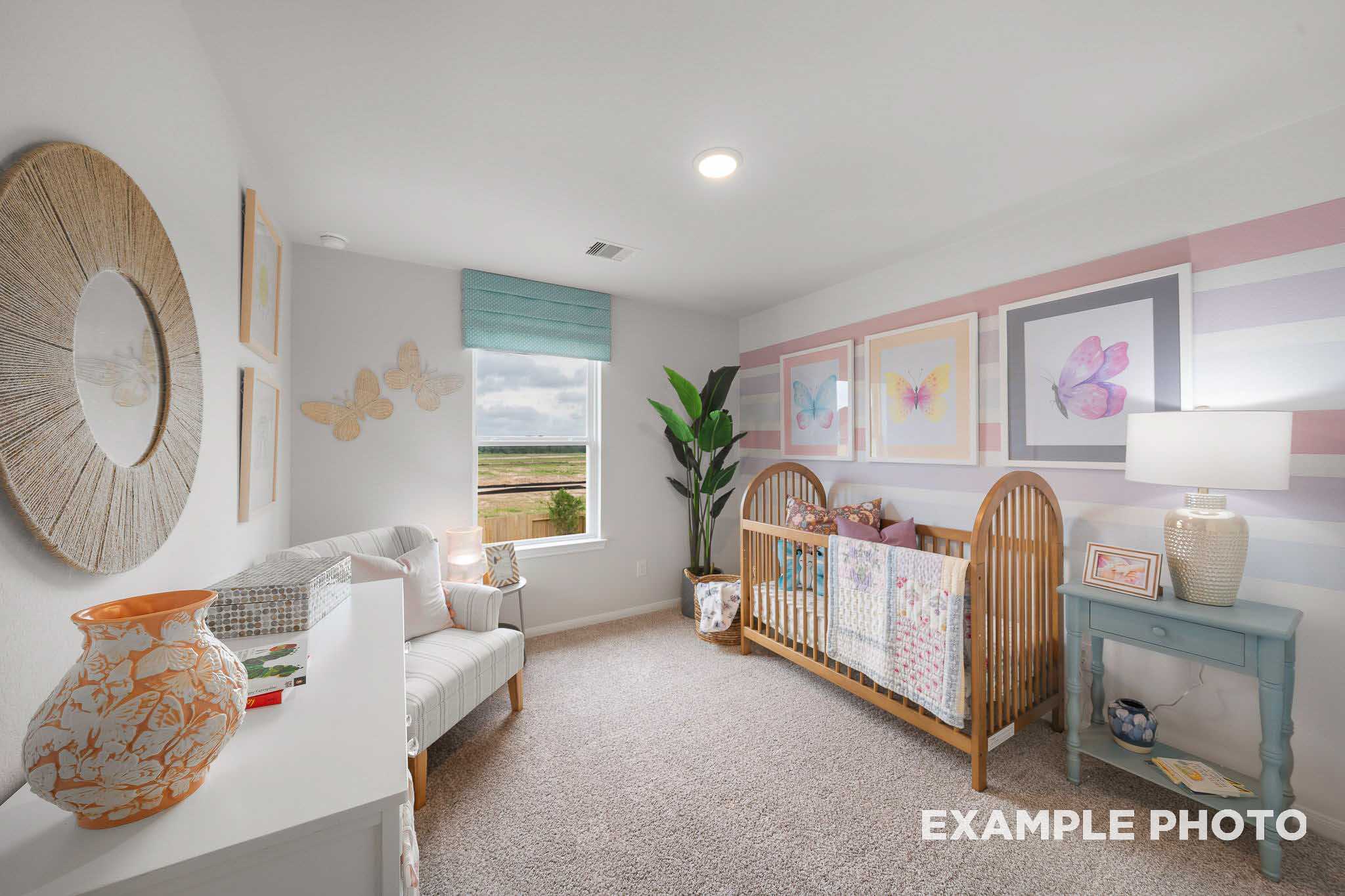 Cozy nursery in The Trinity floor plan with wooden crib, pink accents, butterfly art, and scenic window view