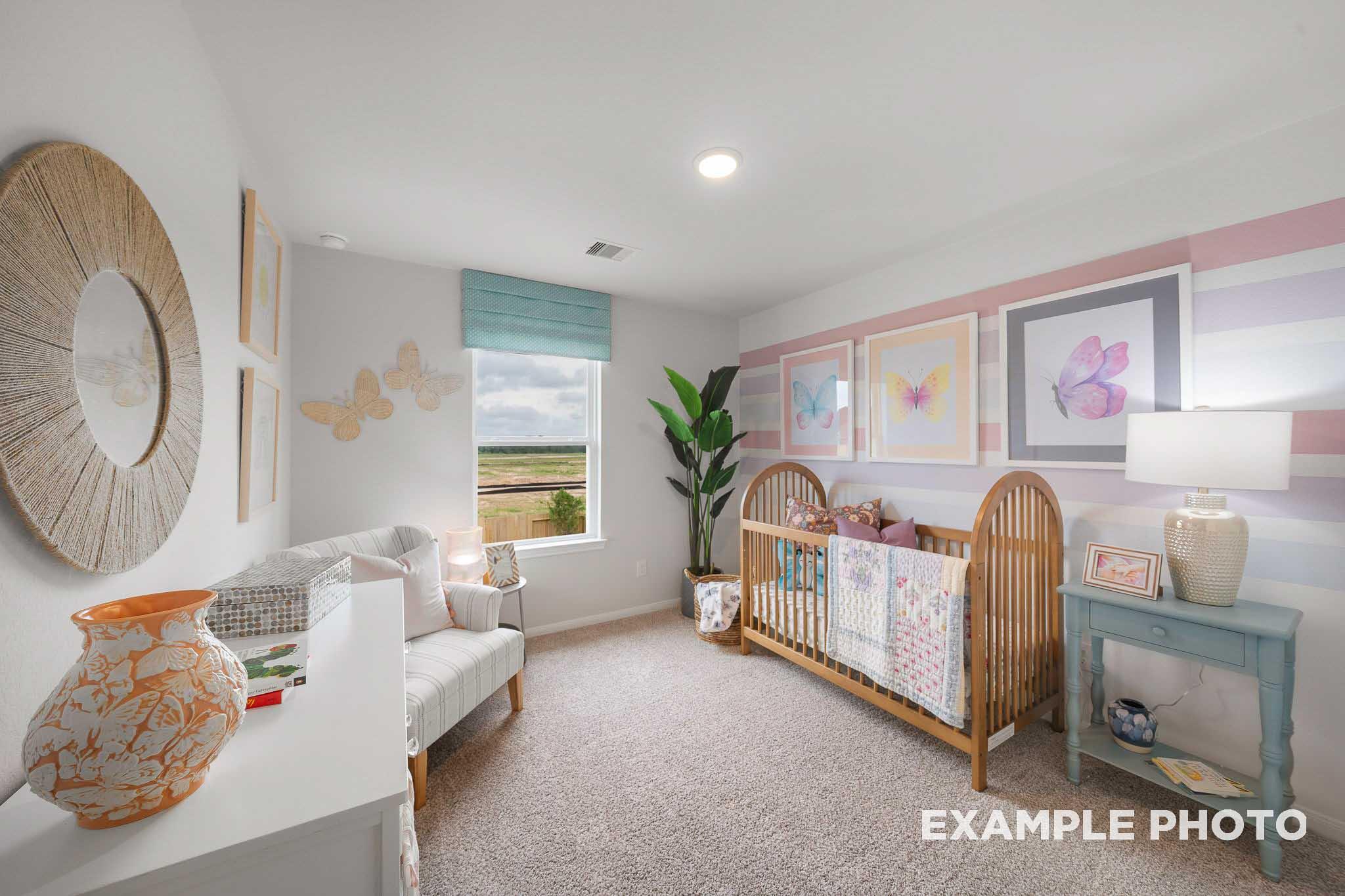 Cozy nursery in The Trinity E home featuring wooden crib, pink striped walls, rocking chair, and prairie view window