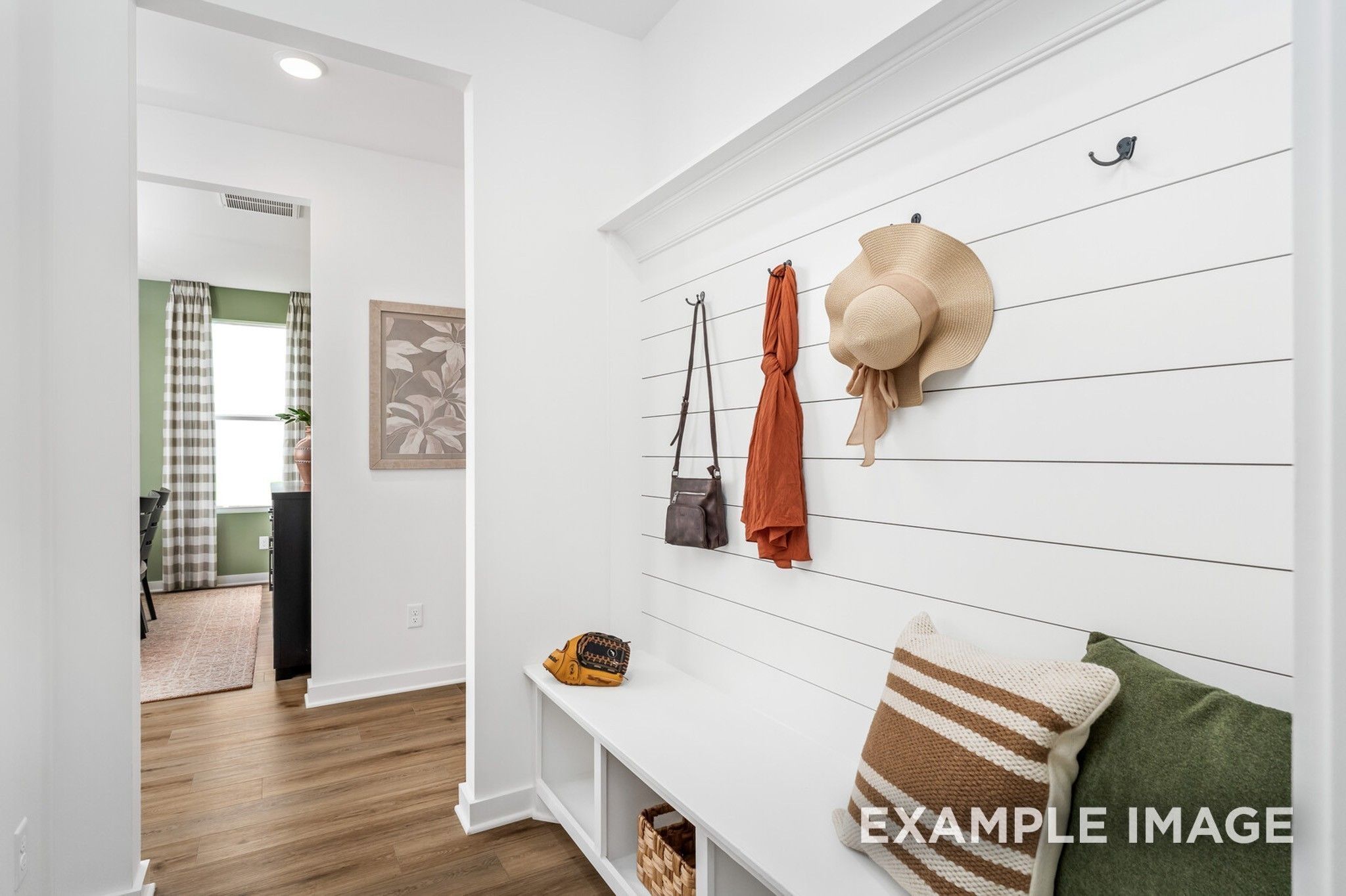 White shiplap mudroom with built-in bench, pillows, hooks holding straw hat and purses in Davidson Homes The Ash A, Gallatin, TN