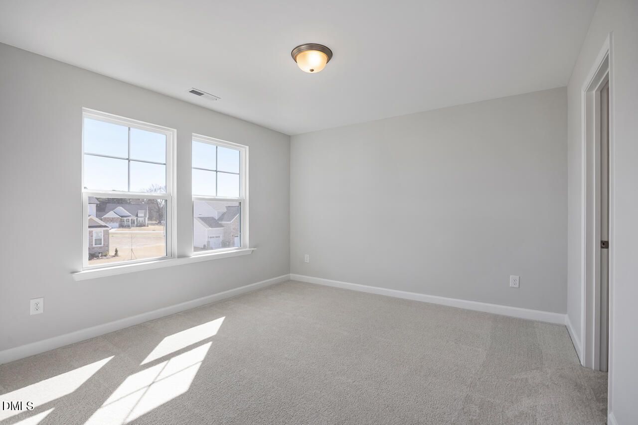 Bright secondary bedroom with light gray walls, neutral carpet, large sunny windows in Davidson Homes The Willow G, Angier, NC
