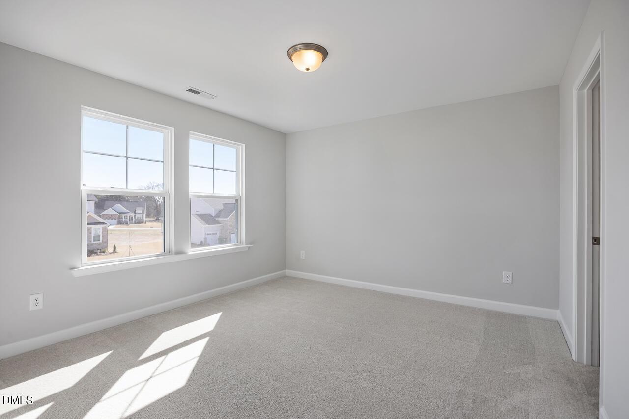 Bright secondary bedroom with light gray walls, neutral carpet, large sunny windows in Davidson Homes The Willow G, Angier, NC
