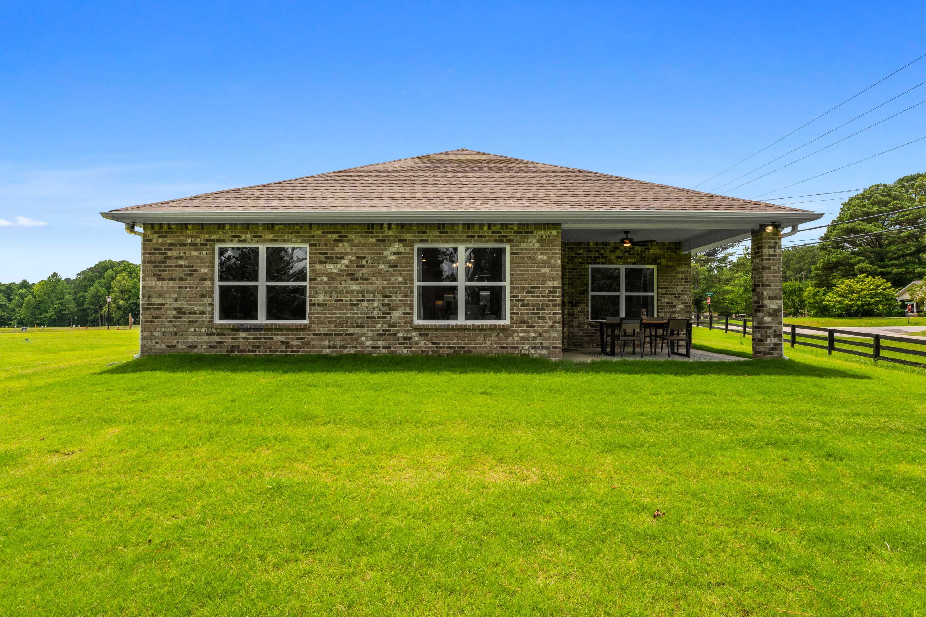 Brick home exterior with covered rear porch, patio seating, lush green lawn and trees at The Highlands in Arab, Alabama