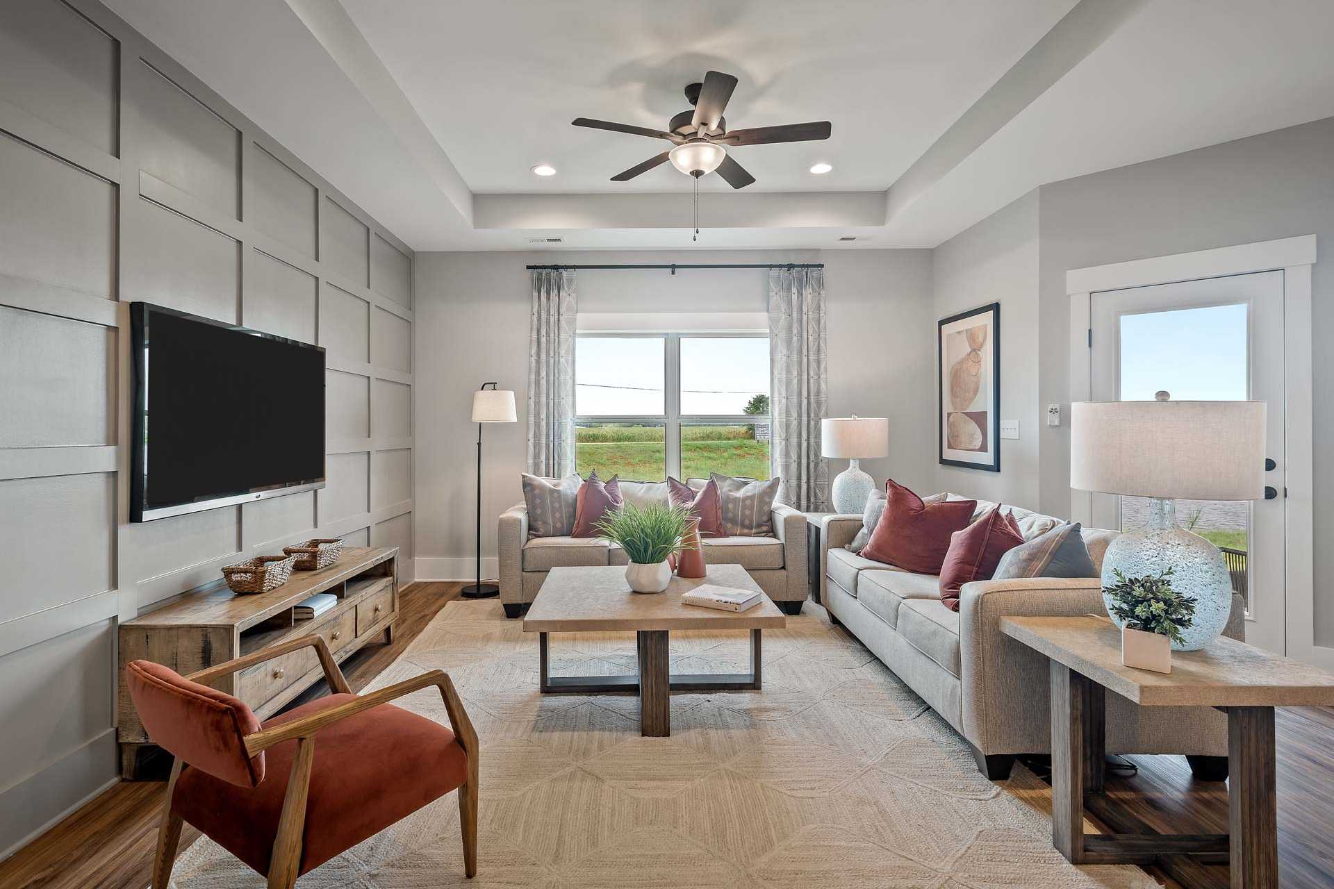 Cozy living room at Heritage Lakes in New Market Alabama with mounted TV on shiplap wall, beige sectional sofa, ceiling fan, and large windows