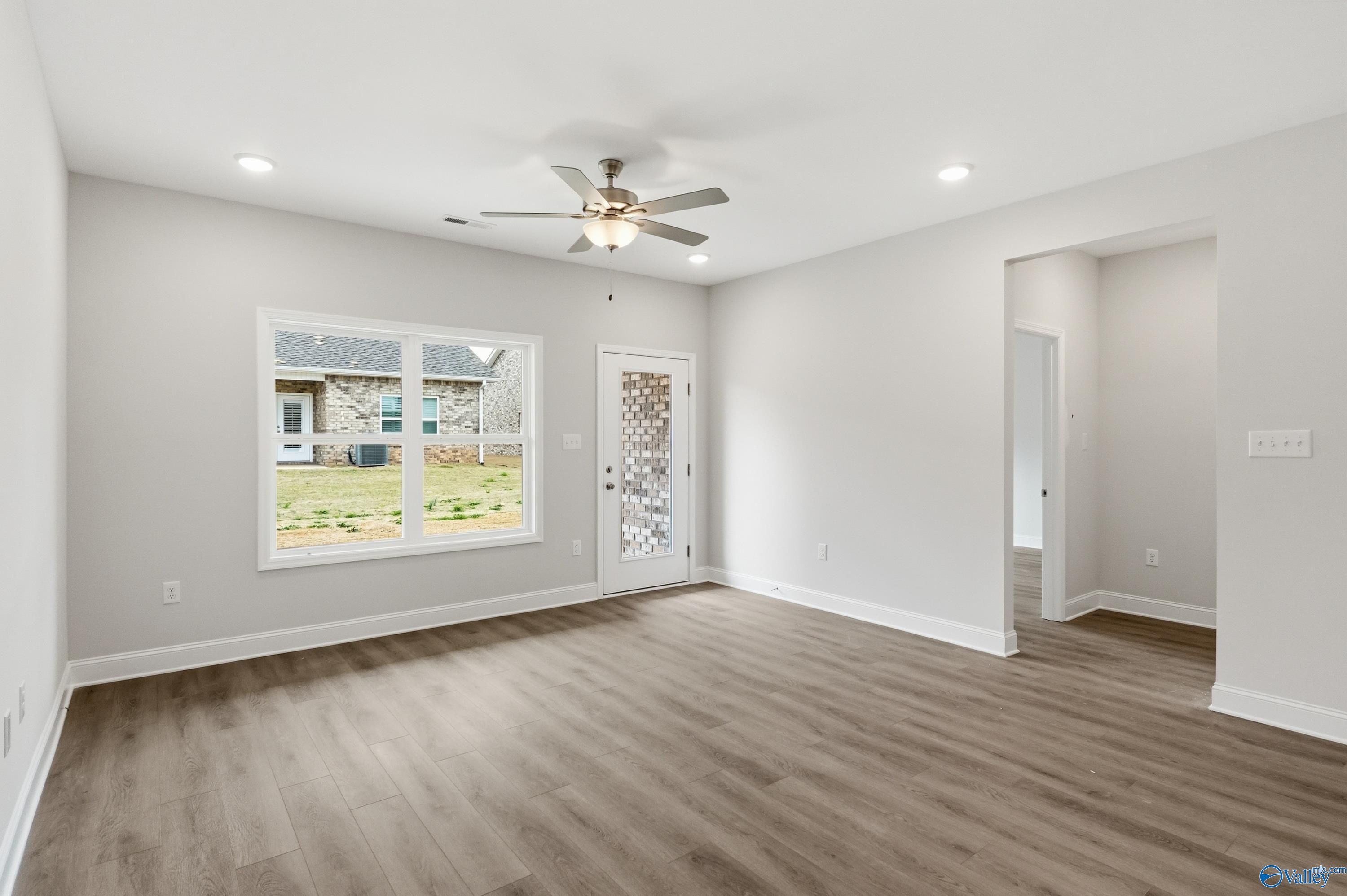 Bright living room with ceiling fan, large window to grassy yard, wood floors and neutral walls in Davidson Homes Cumberland, Decatur AL