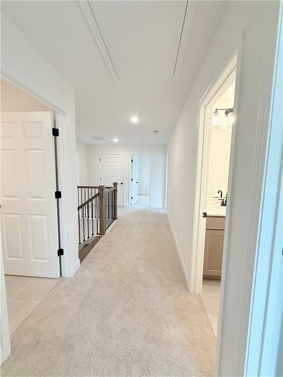 Bright upstairs hallway with carpet flooring and access to bedrooms in The Hickory B floor plan at Wehunt Meadows.