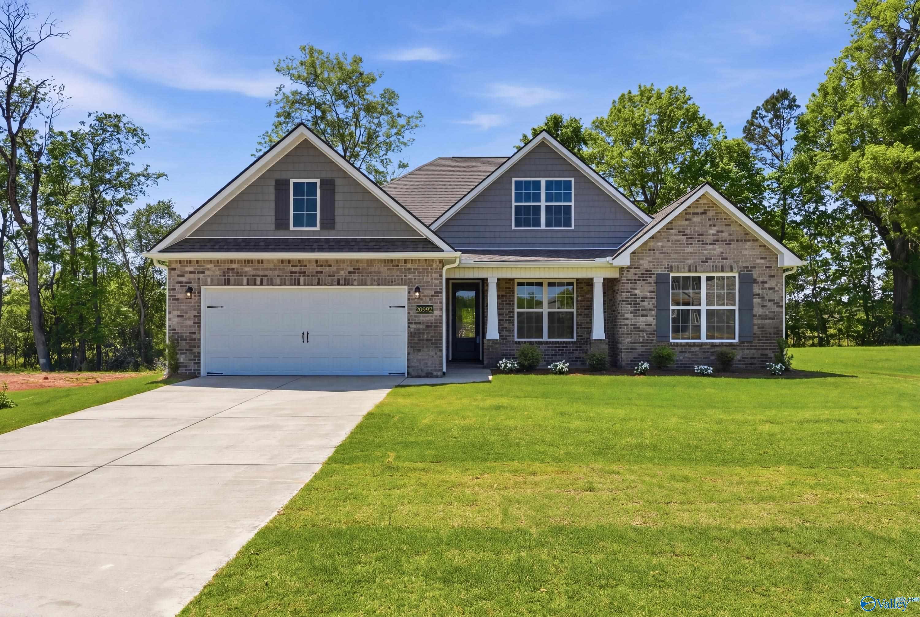 Gray brick and siding single-story home with 2-car garage, front porch, and lush lawn in The Meadows, Athens, Alabama
