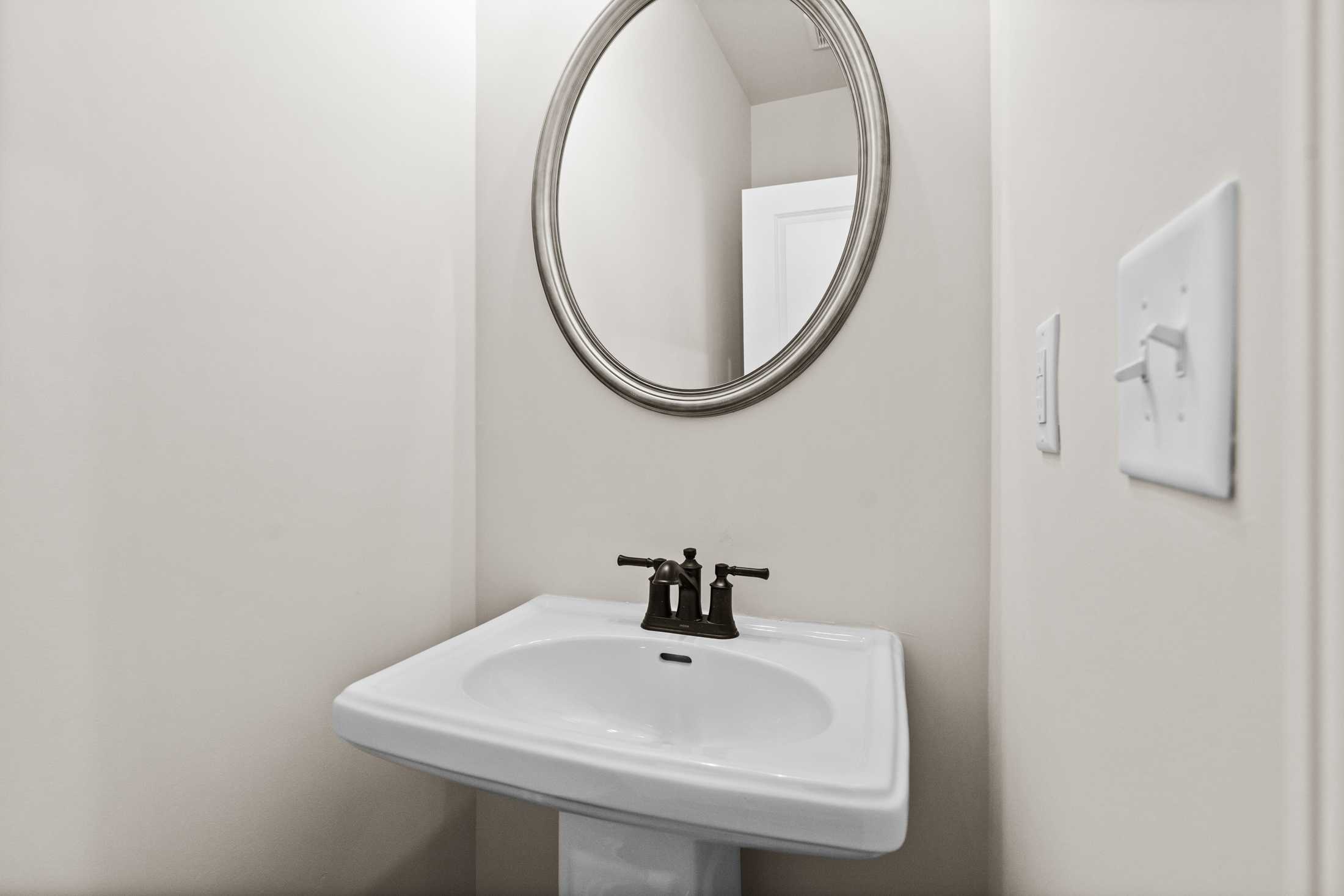 The Glenwood B powder room featuring white pedestal sink, oval mirror, neutral walls in Davidson Homes design