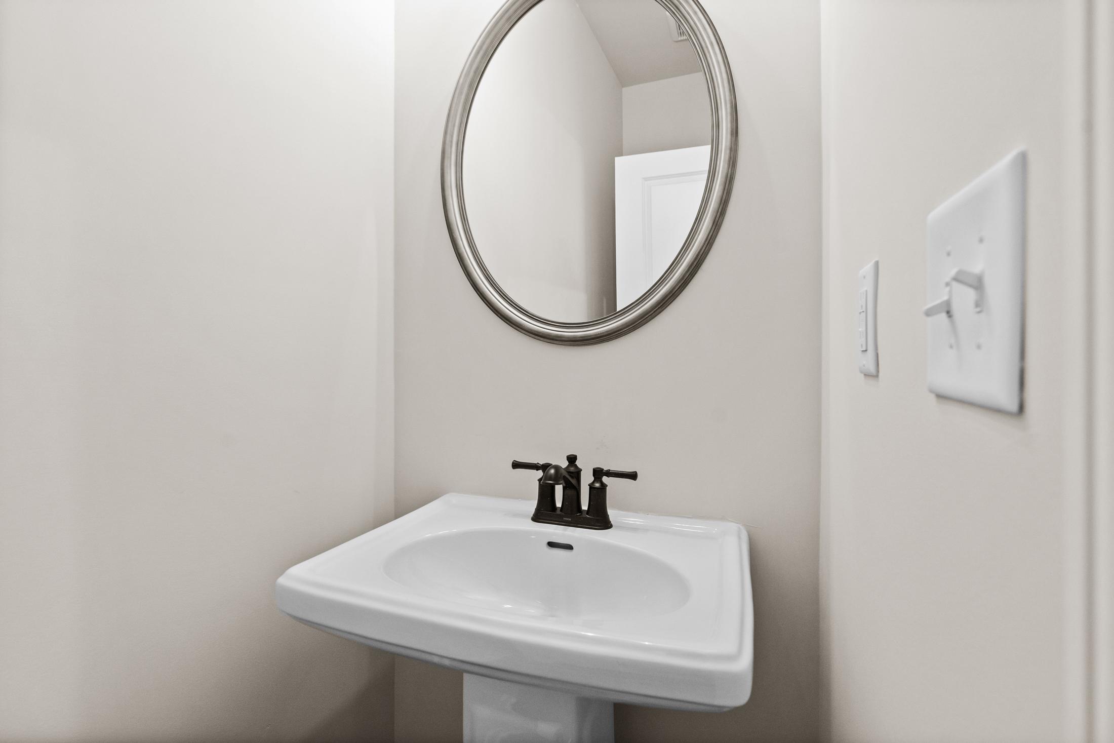 The Glenwood powder room featuring white pedestal sink, chrome faucet, and oval mirror in neutral tones