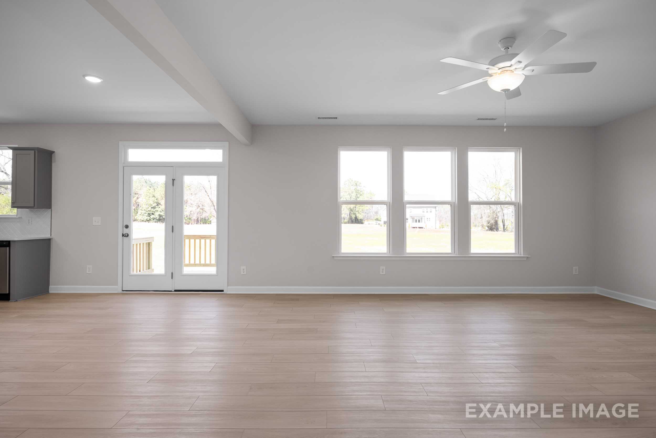 Spacious great room in The Hickory II featuring hardwood floors, large windows, French doors to deck, and ceiling fan