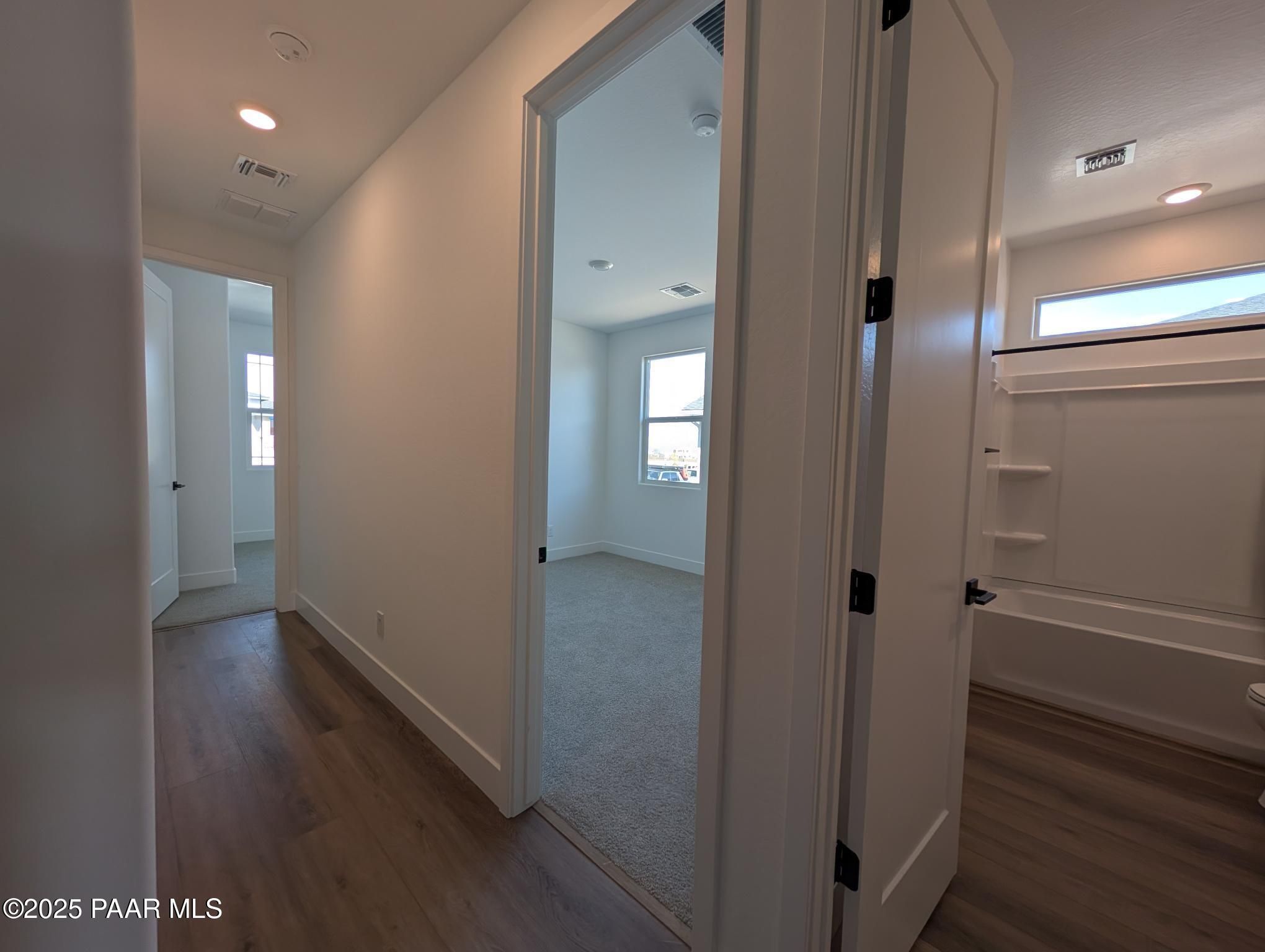 Bright hallway leading to carpeted bedroom and bathroom with tub in Davidson Homes The Sheridan II F, Prescott, Arizona