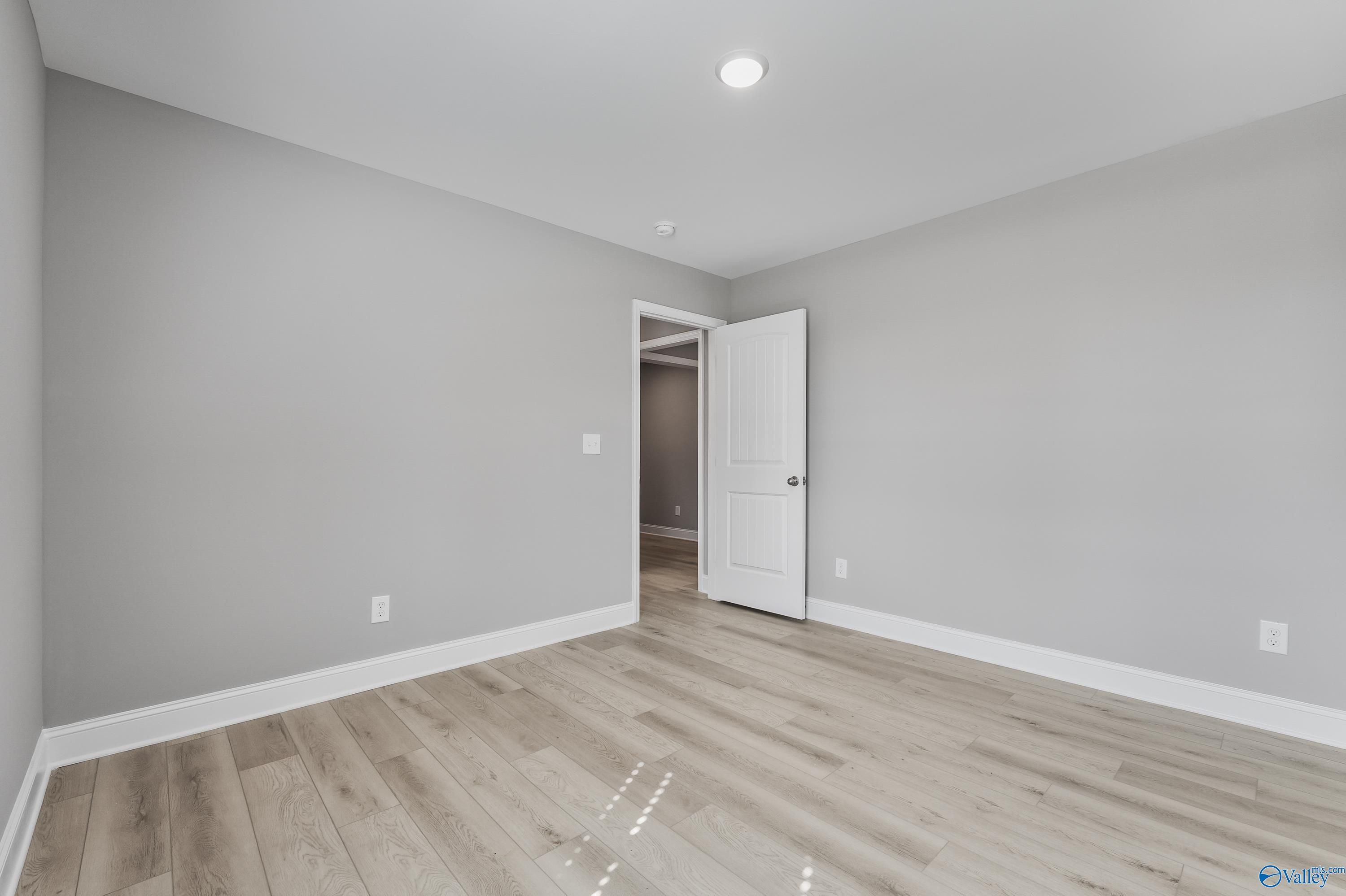 Spacious empty bedroom with light gray walls, open white door, and hardwood floors in Davidson Homes The Everett B, Athens, Alabama