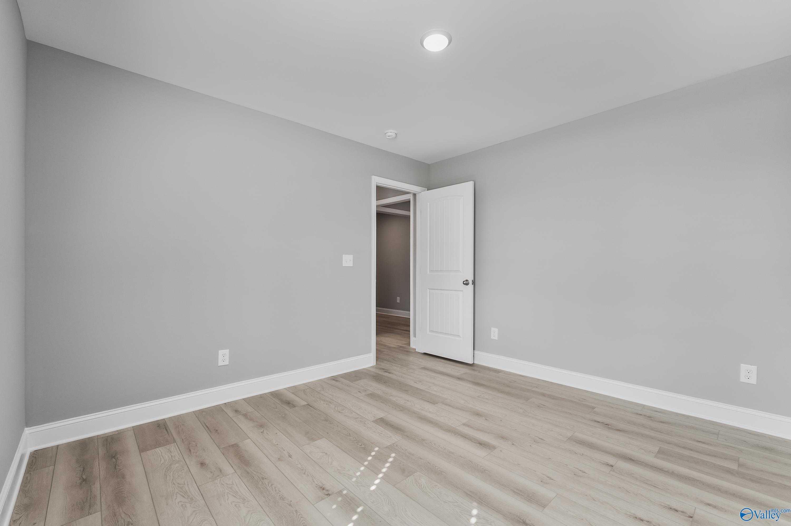 Spacious empty bedroom with gray walls, open white door to ensuite, and laminate wood floors in The Everett B, Athens, AL
