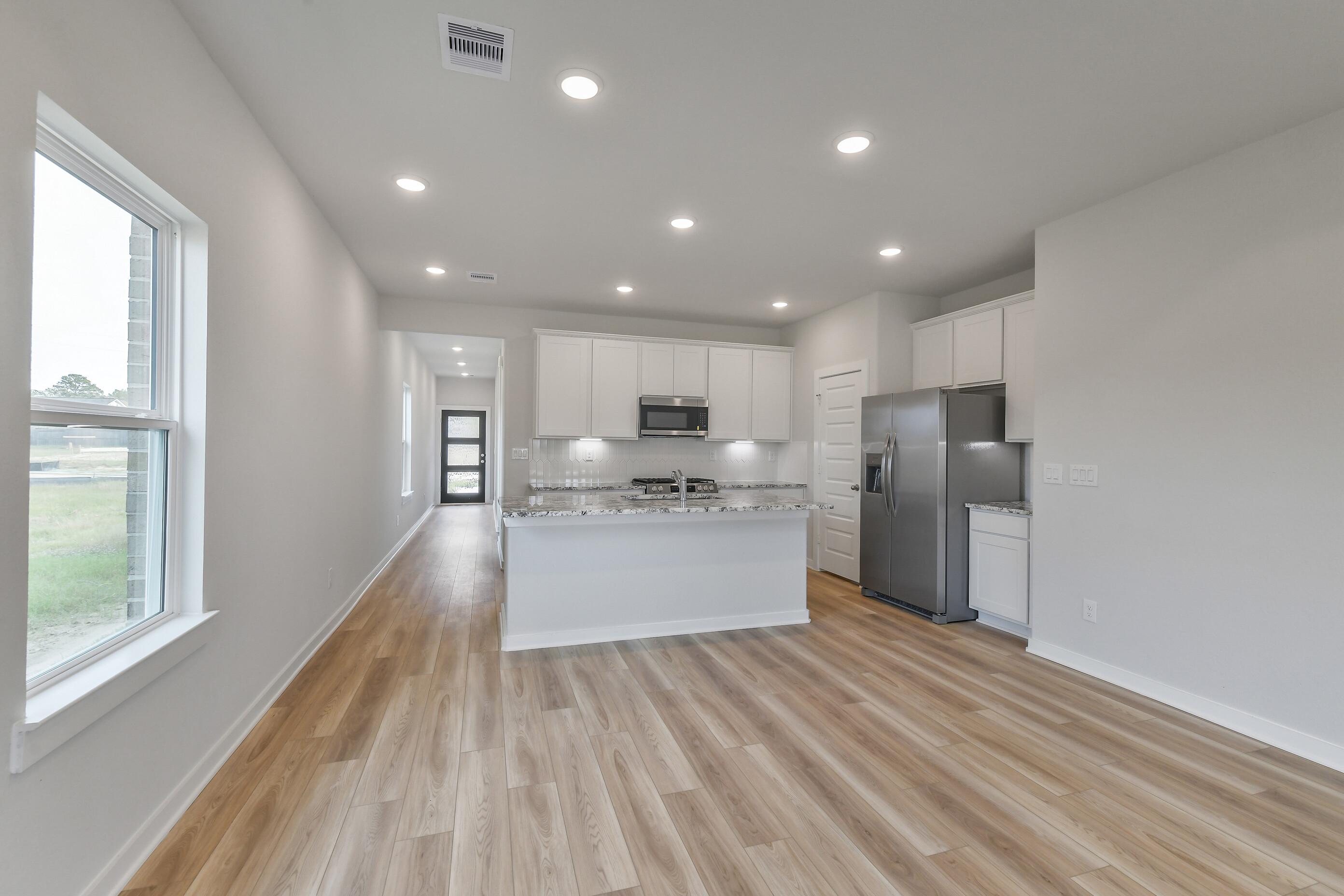 Open-concept kitchen with white shaker cabinets, quartz island, stainless appliances, and hallway view in Davidson Homes Colorado G, Magnolia TX