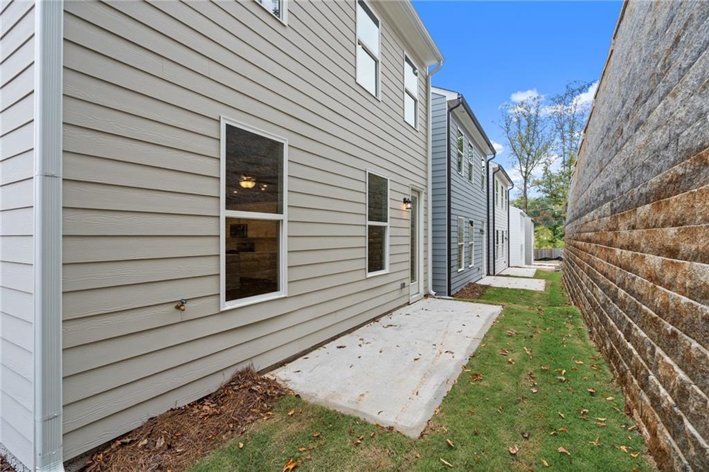 Side view of The Marion B two-story home with gray siding, concrete patio, lush grass, and wooden fence in The Village at Shallowford, Kennesaw