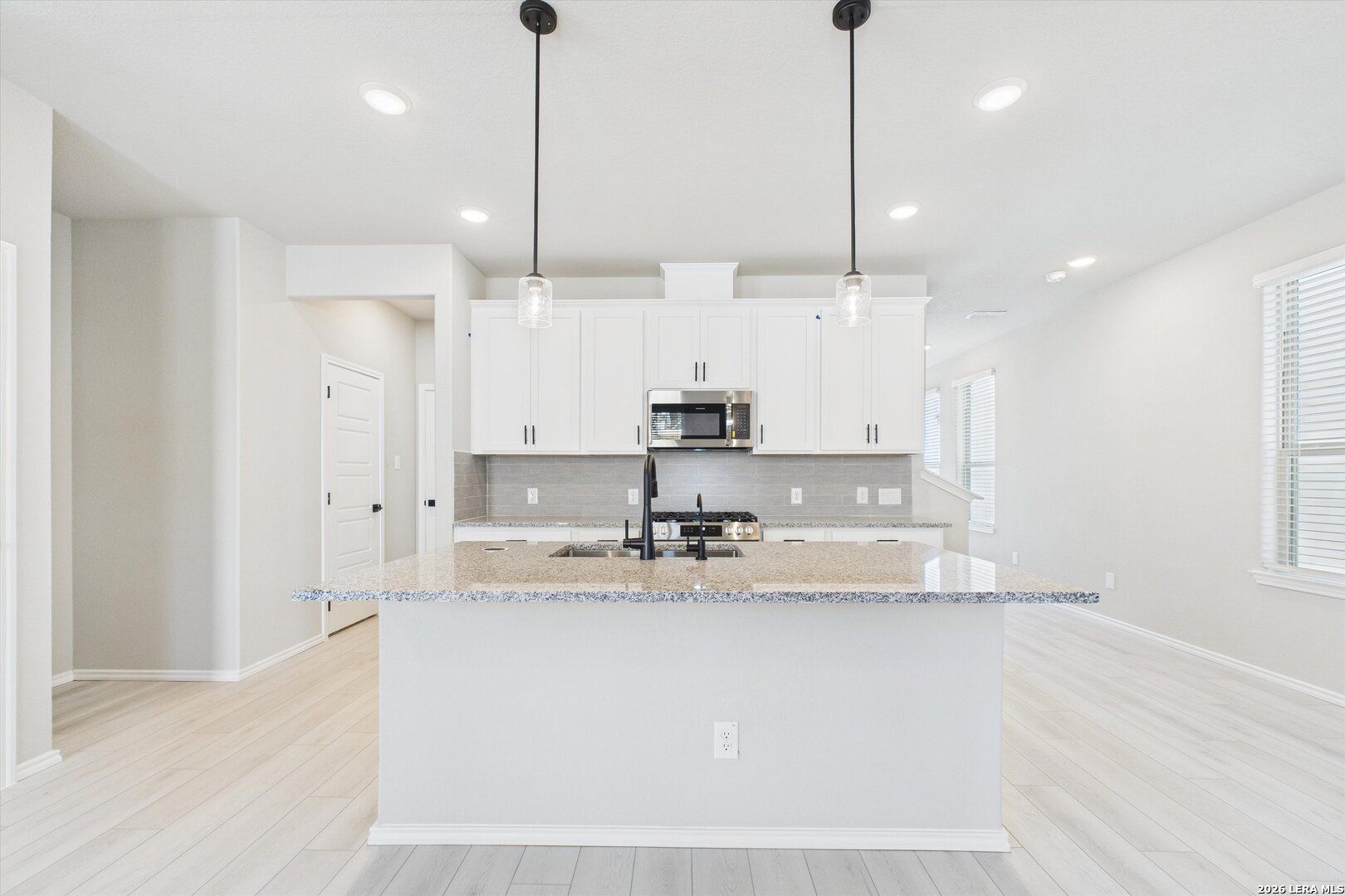 Modern open-concept kitchen with white cabinets, granite island, stainless appliances in Davidson Homes Charlotte A, San Antonio