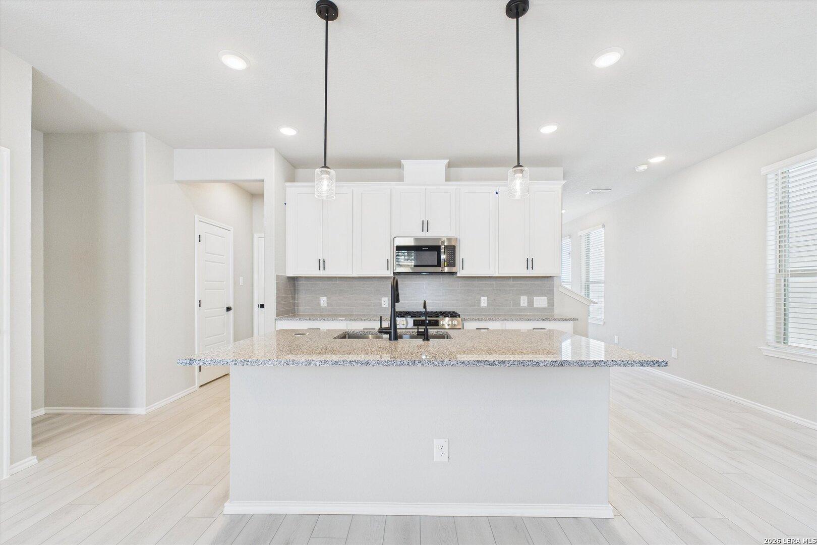 Modern open-concept kitchen with white cabinets, granite island, stainless appliances in Davidson Homes Charlotte A, San Antonio