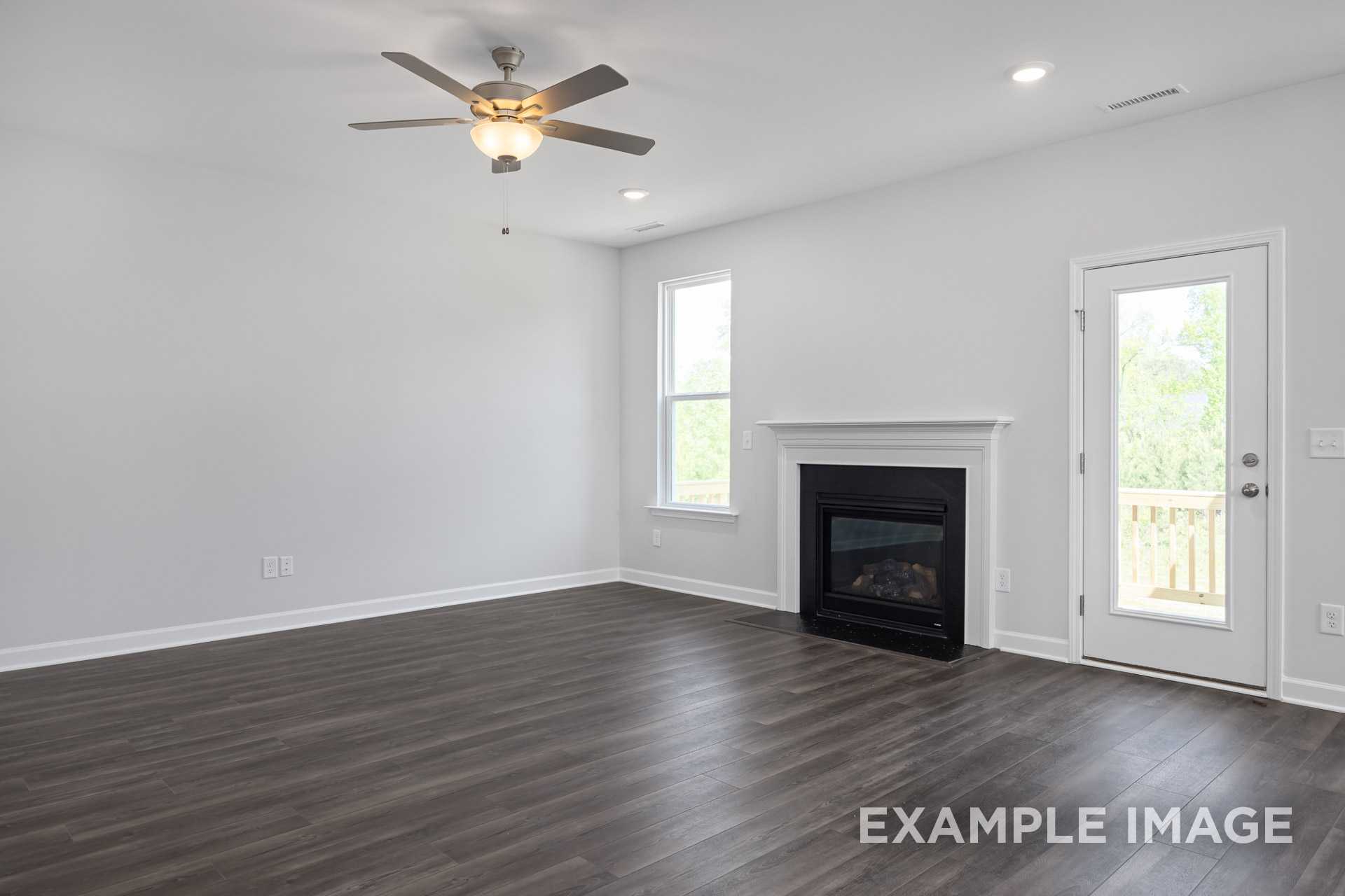 Spacious living room in The Grace C with gas fireplace, ceiling fan, large windows, and French doors to deck