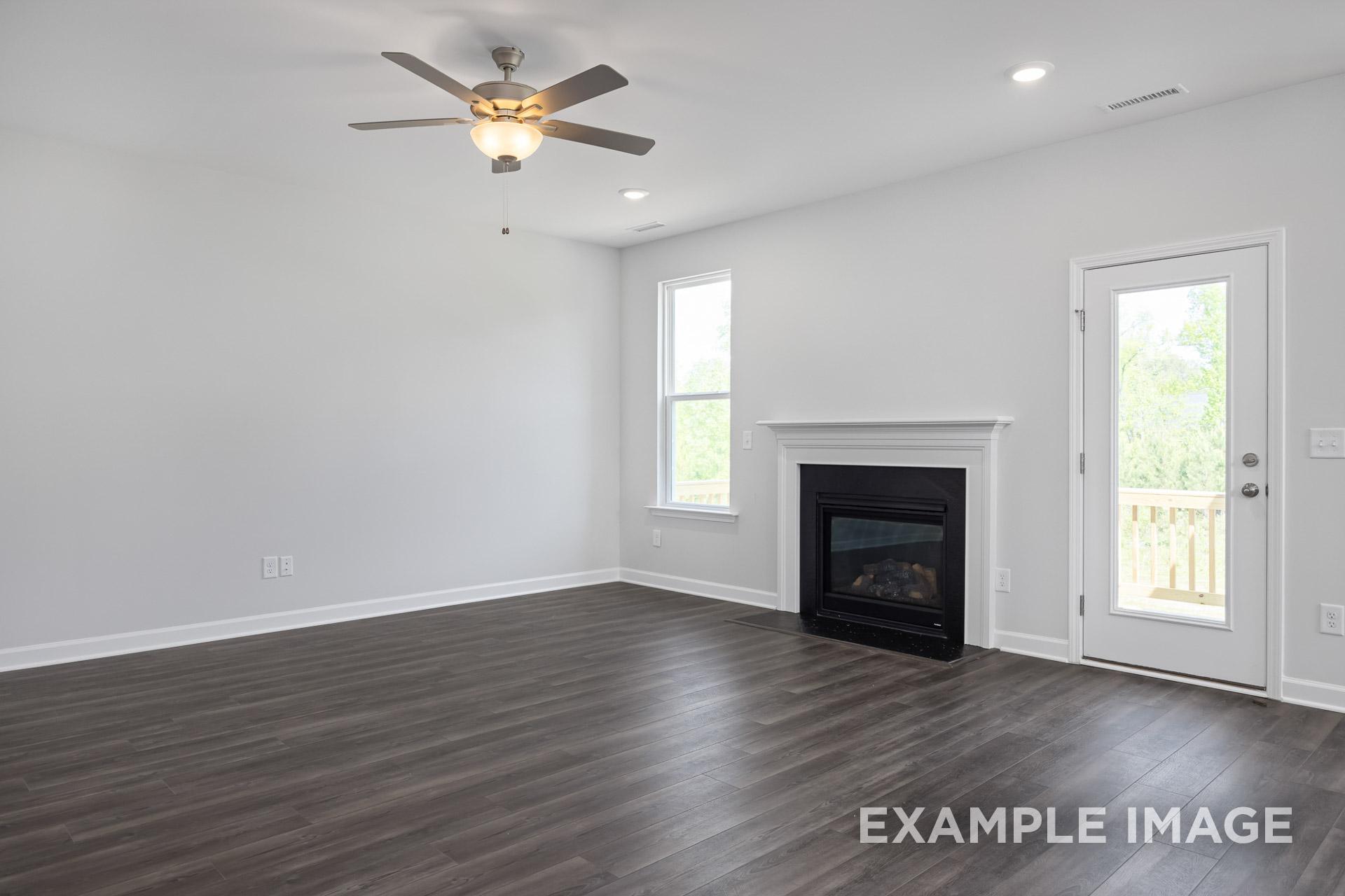 Spacious living room in The Grace C with gas fireplace, ceiling fan, large windows, and French doors to deck