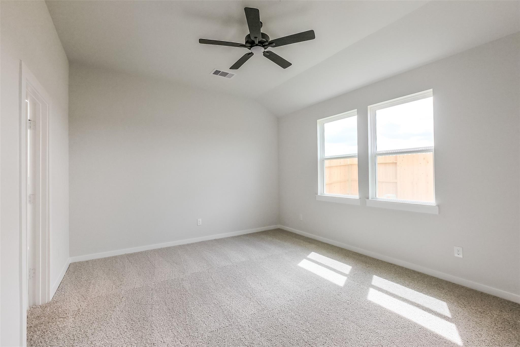 Bright secondary bedroom with ceiling fan, beige walls, carpet floor, and sunny windows in Davidson Homes The Tierra B, Emberly, Beasley, Texas