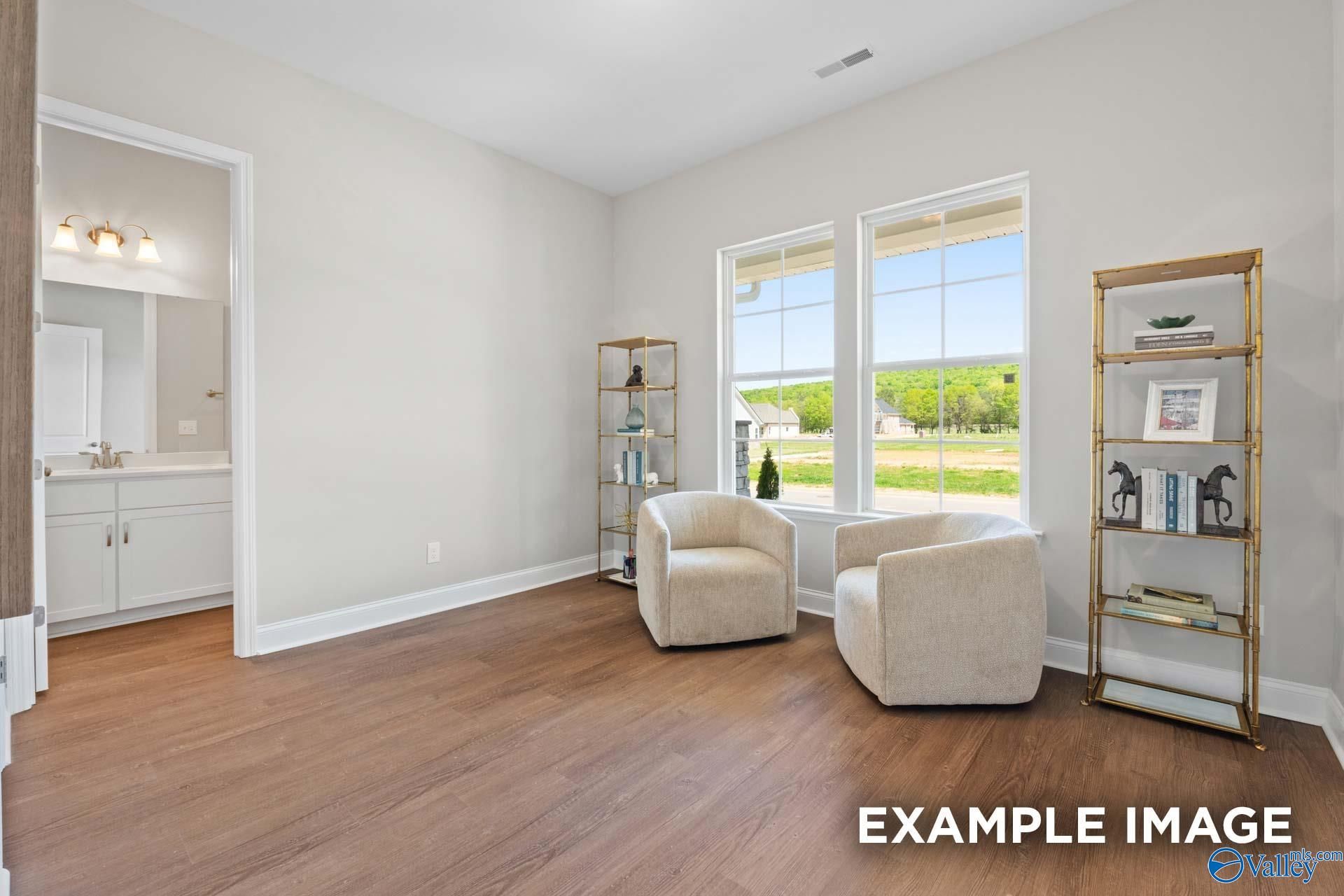 Cozy sitting area with cream armchairs, gold etagere bookshelf, and en-suite bathroom in Evermore Homes The Haven E, Owens Cross Roads, Alabama
