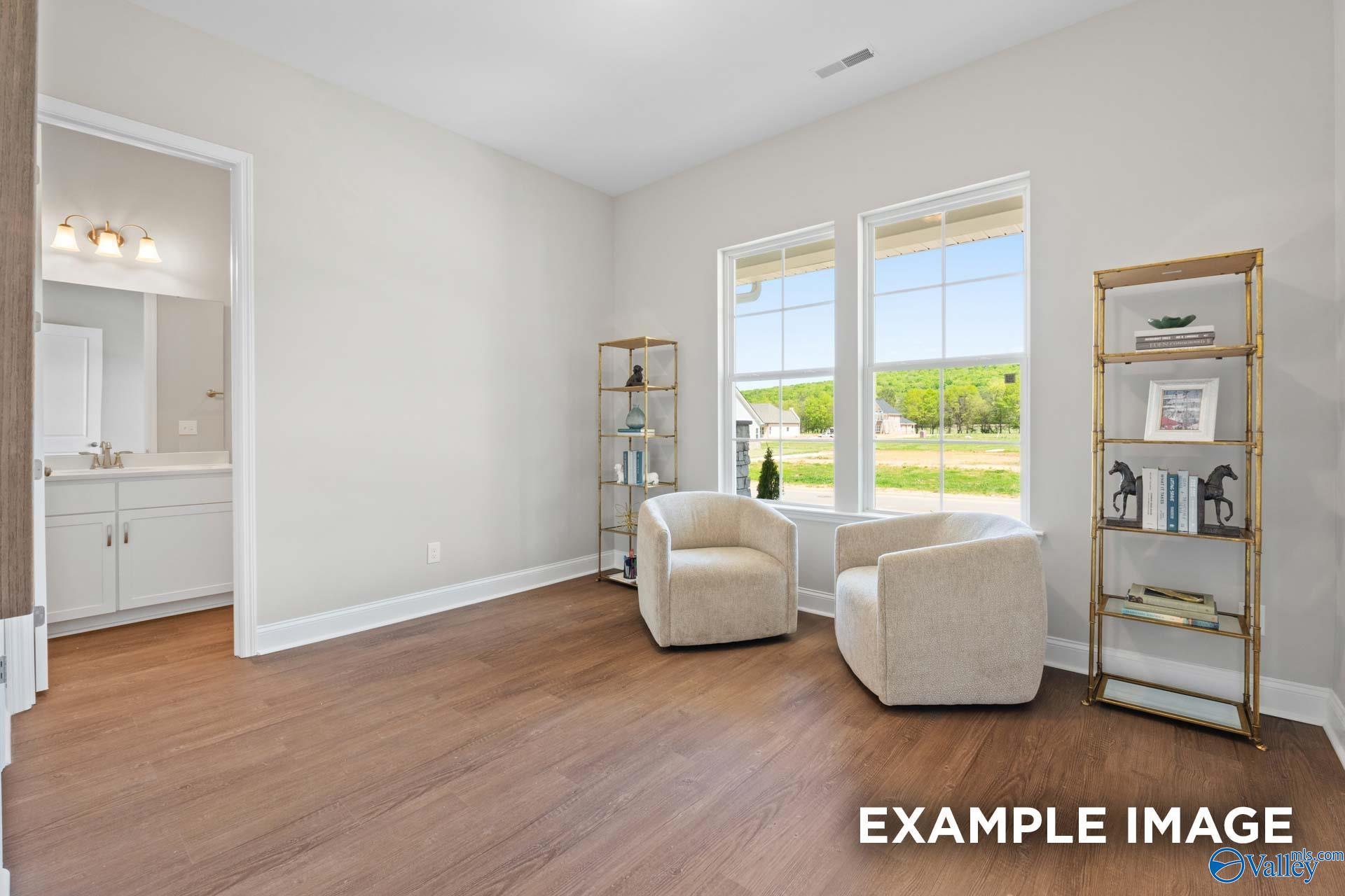 Cozy sitting area with cream armchairs, gold etagere bookshelf, and en-suite bathroom in Evermore Homes The Haven E, Owens Cross Roads, Alabama