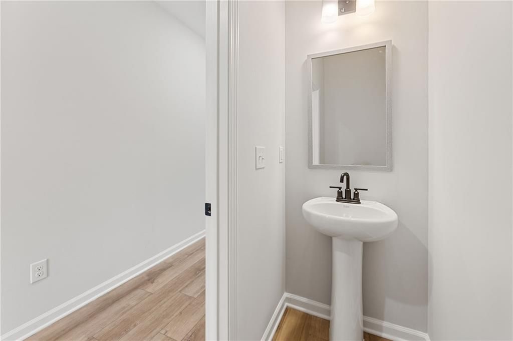 Modern powder room with white pedestal sink, framed mirror, and wood flooring in The Rabun C by Davidson Homes, Winder, GA