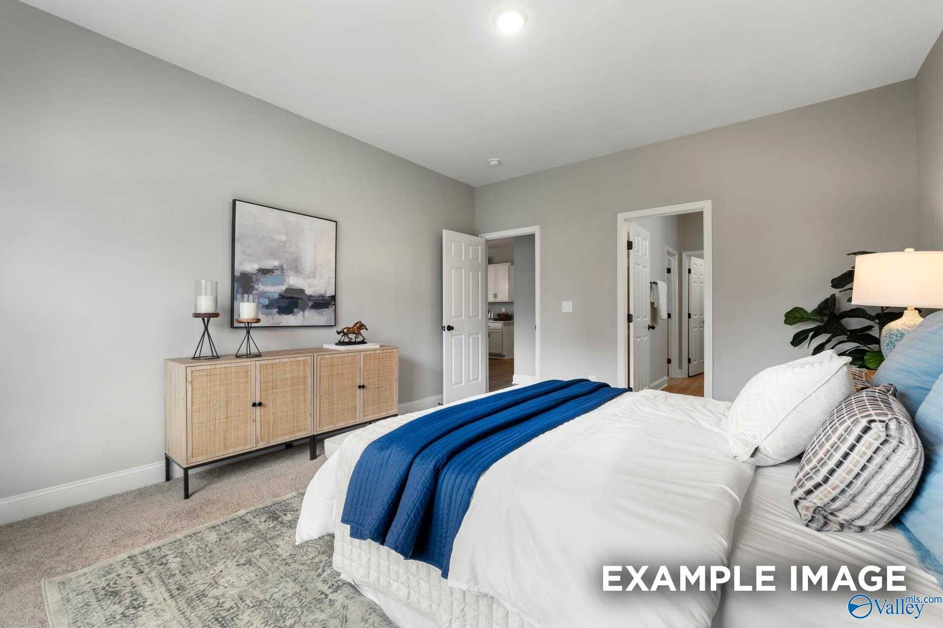 Serene master bedroom with white bedding, blue throw, rattan dresser, abstract art, and en-suite bath in Davidson Homes The Daphne C, Owens Cross Roads