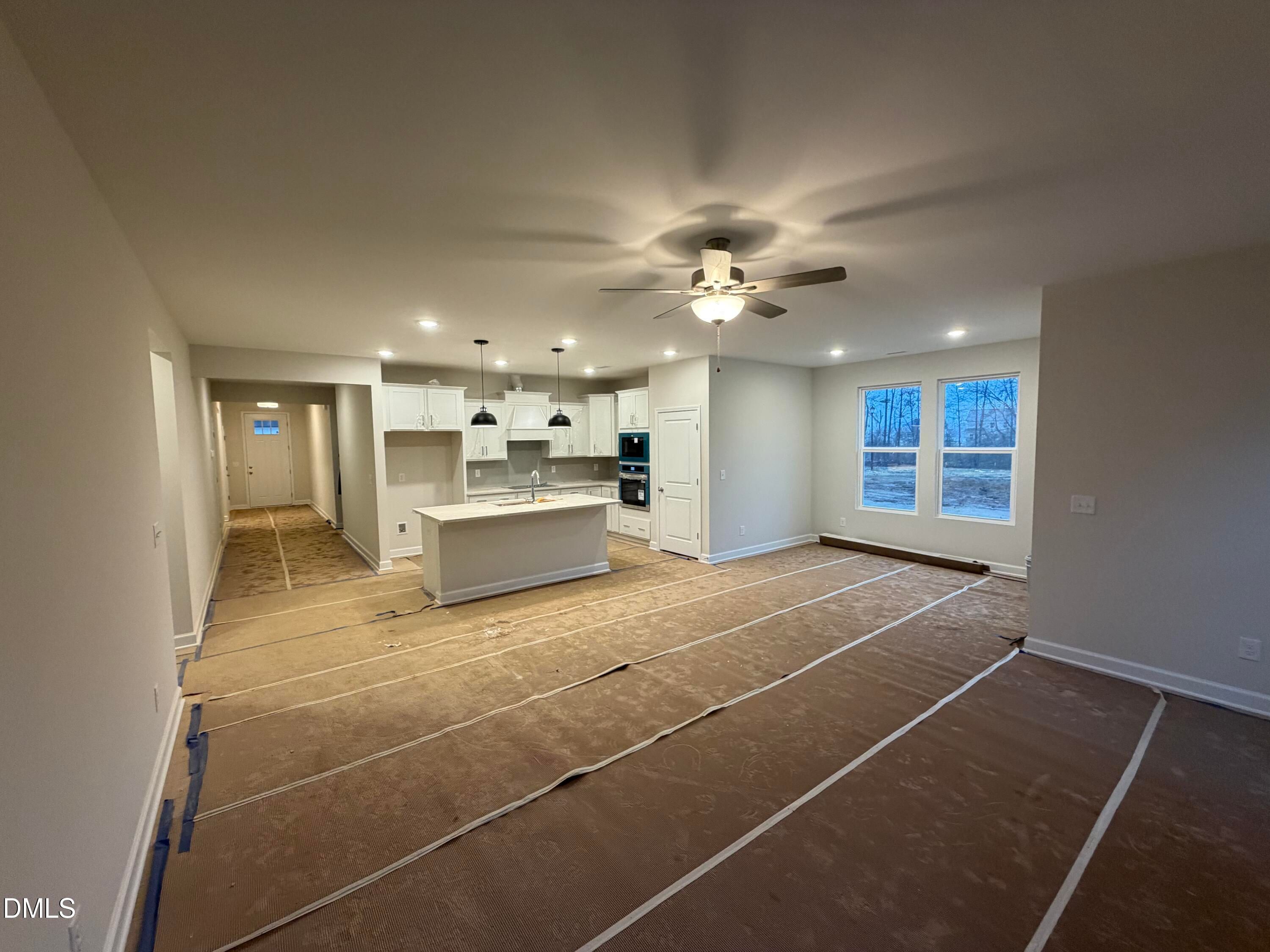 Open-concept kitchen and living area with white cabinets, island, and large windows in unfinished The Daphne C home, Lillington, NC