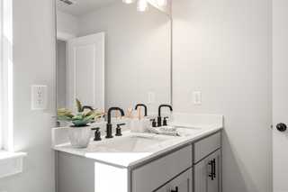 Modern master bathroom in The Washington H townhome with double vanity, black faucets, gray cabinets, and plants