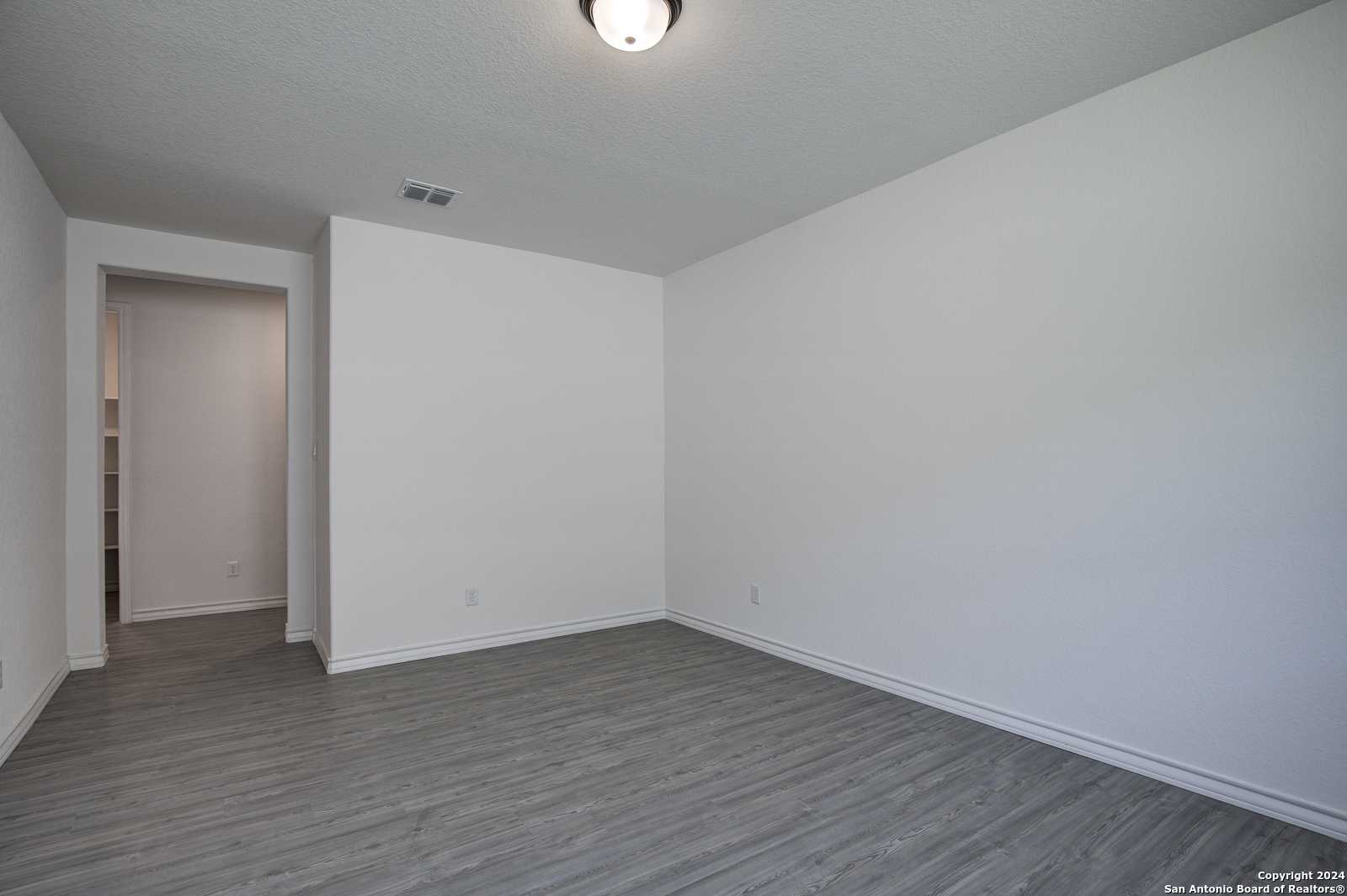 Empty versatile room featuring white walls, gray laminate flooring, built-in pantry, and open doorway in Davidson Homes The Garner B, Castroville, Texas