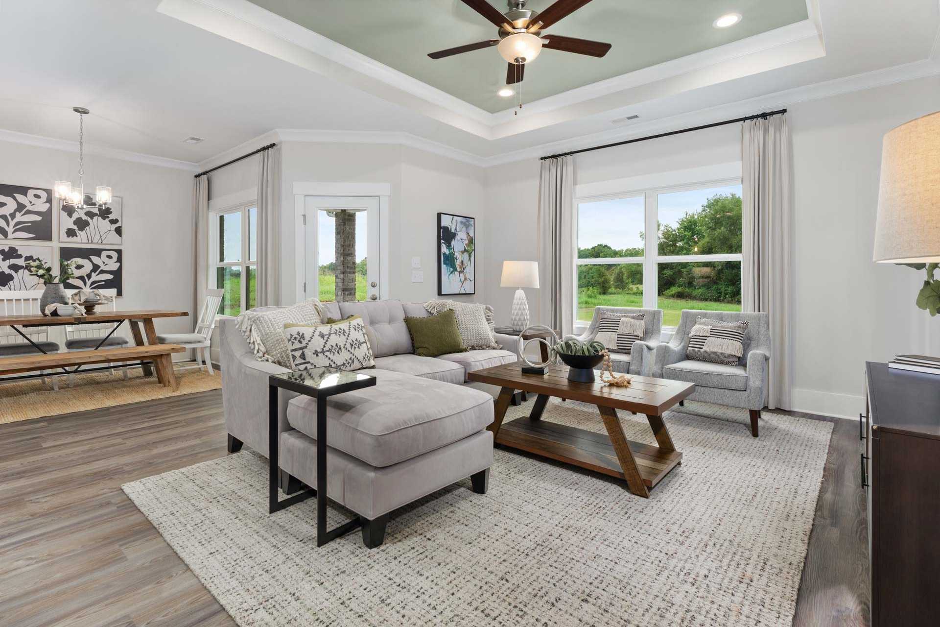 Open-concept living and dining room at The Meadows in Athens AL with hardwood floors, gray sectional sofa, and large windows overlooking greenery