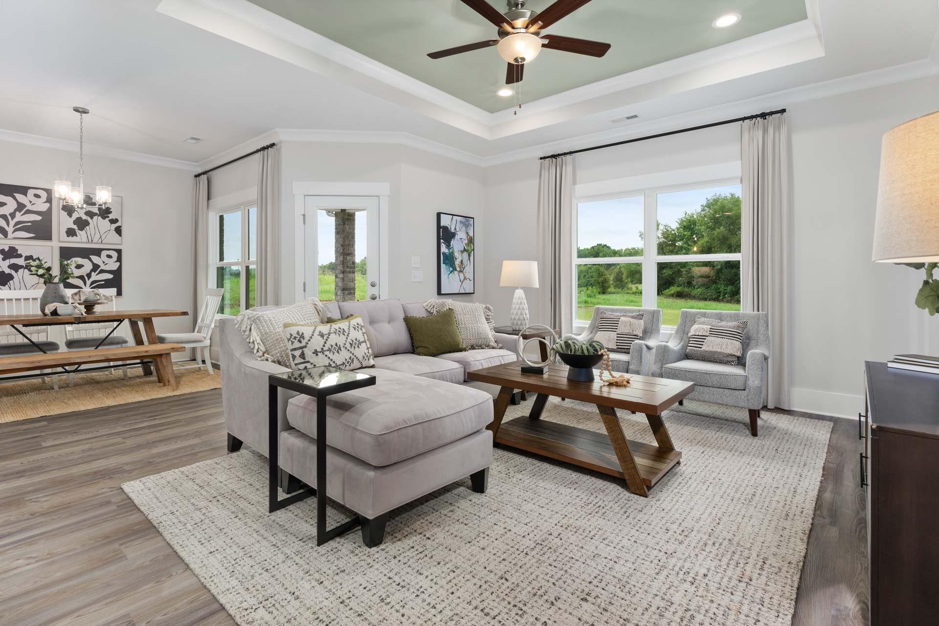 Open-concept living and dining room at The Meadows in Athens AL with hardwood floors, gray sectional sofa, and large windows overlooking greenery