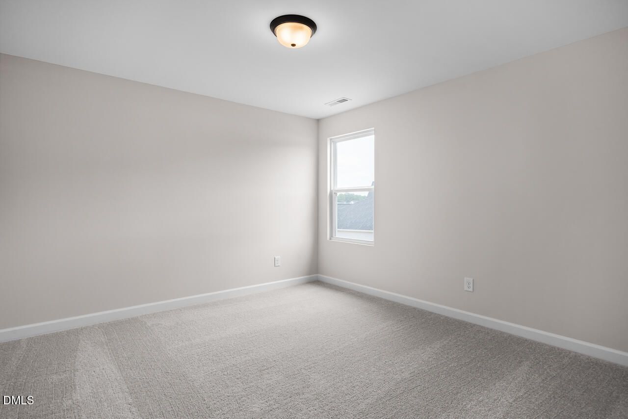 Bright, carpeted bedroom with neutral walls in The Willow B floor plan at Woodland Crossing in Zebulon, North Carolina.