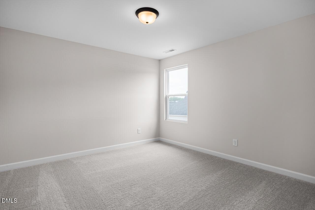 Bright, carpeted bedroom with neutral walls in The Willow B floor plan at Woodland Crossing in Zebulon, North Carolina.