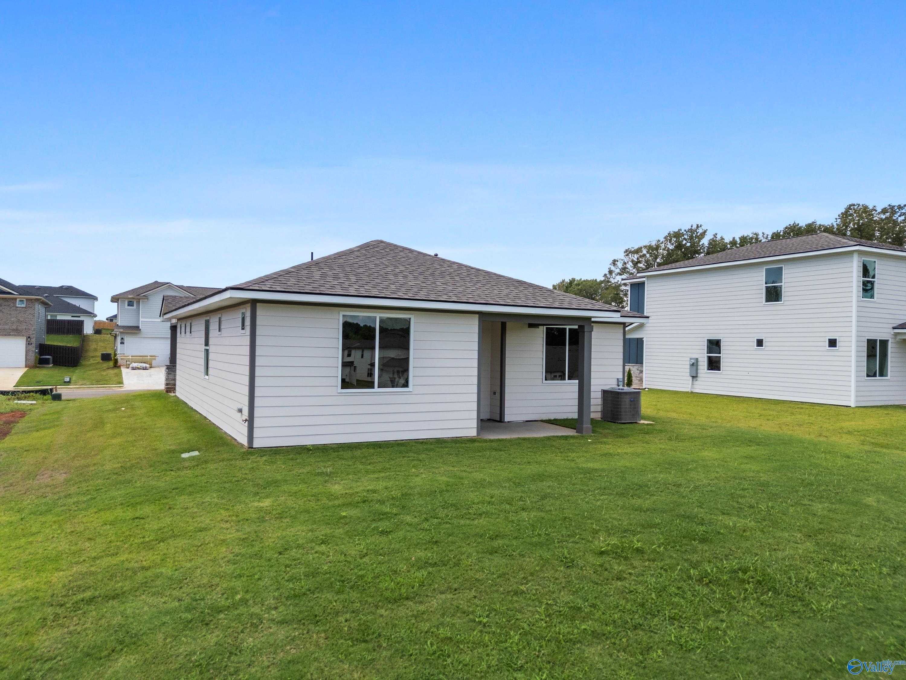 Modern 1-story beige home exterior with covered entry, large windows, and lush green yard in Evergreen Mill, Madison, Alabama