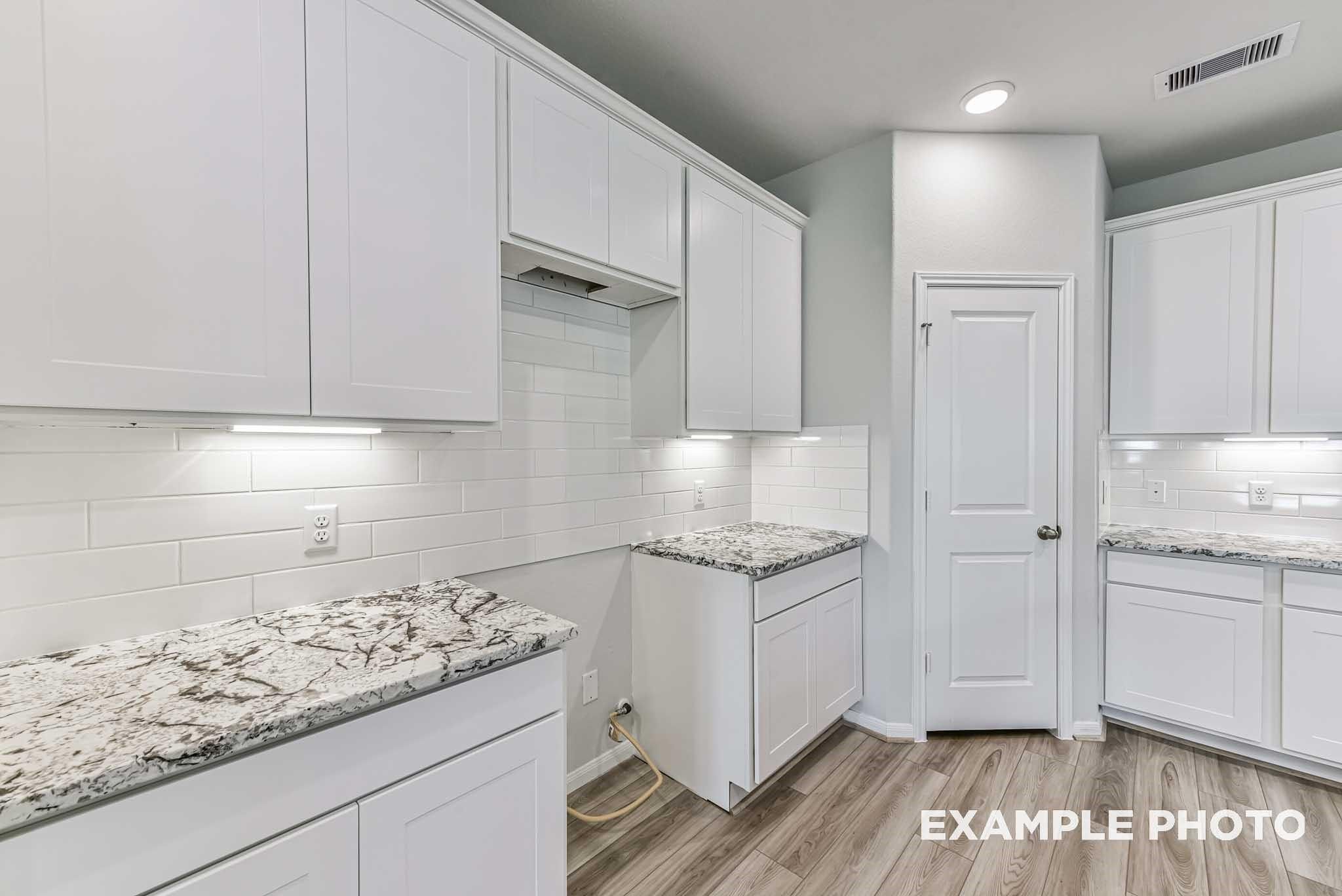 Modern white shaker kitchen with marbled granite counters, subway tile backsplash, and under-cabinet lighting in Davidson Homes The Riviera A, Rosharon, Texas