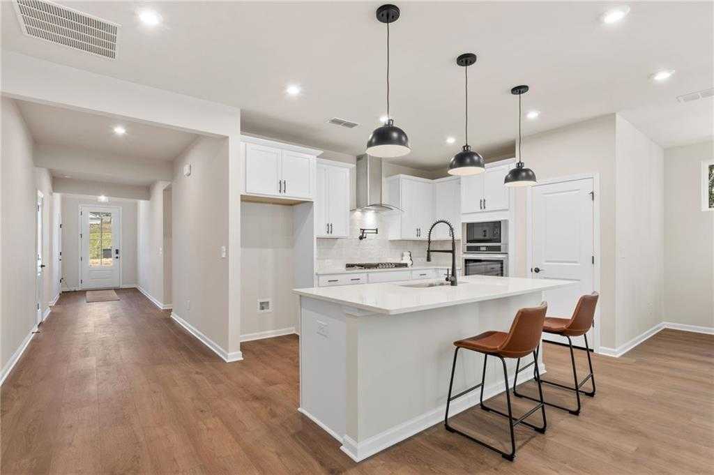 Modern white kitchen with quartz island, bar stools, pendant lights, and open hallway in Davidson Homes The Daphne B, Loganville, GA