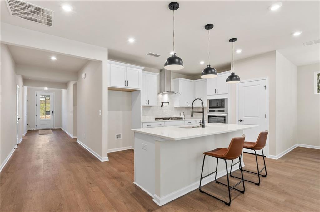 Open-concept white kitchen with quartz island, pendant lights, bar stools, and hardwood floors in Davidson Homes The Daphne B, Loganville, GA