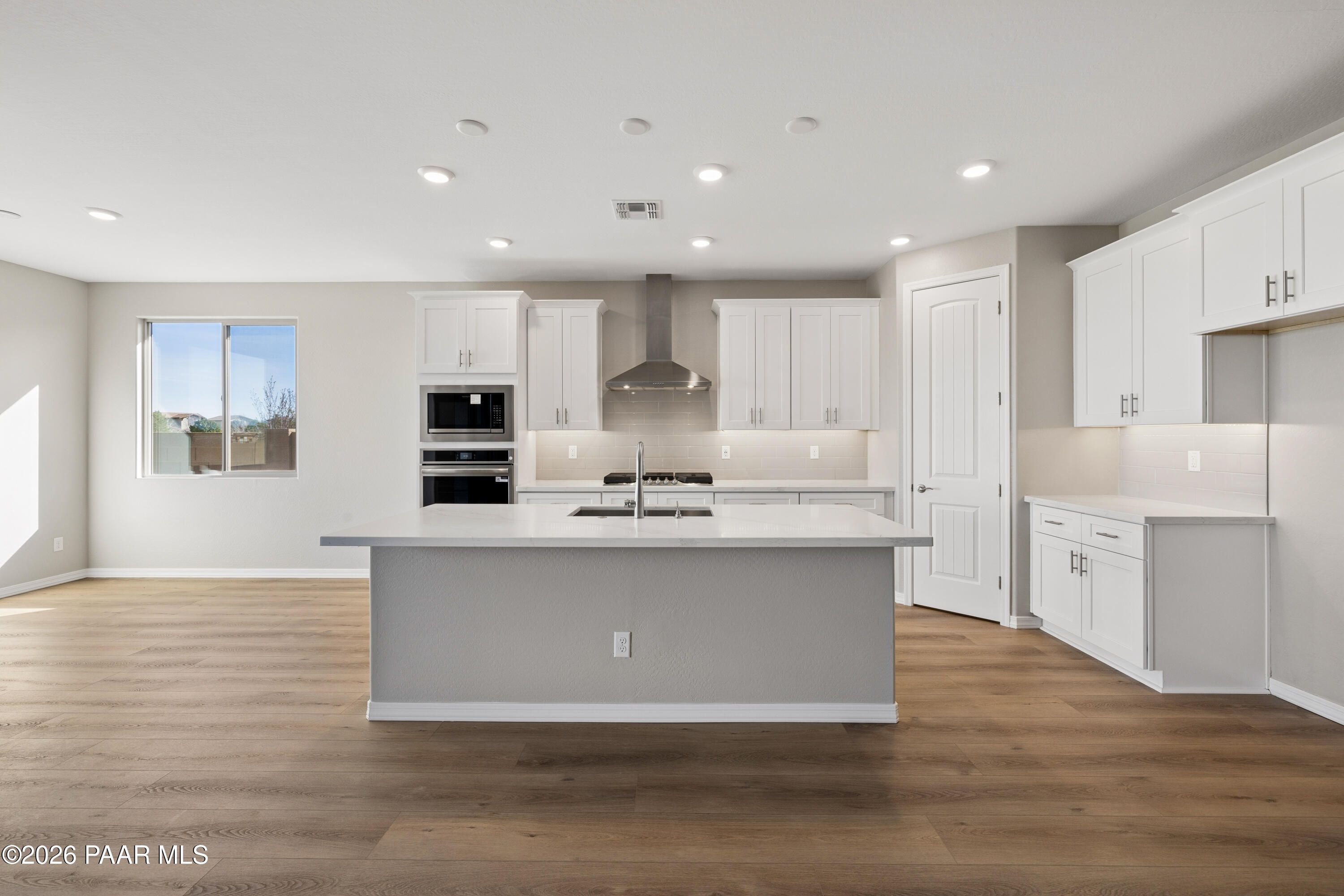 Modern white kitchen with gray quartz island, stainless steel appliances, and hardwood floors in Davidson Homes The Harmony A, Prescott Valley