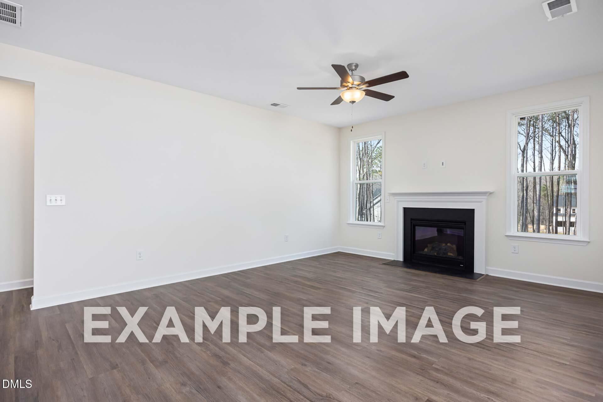 Bright living room with gas fireplace, ceiling fan, large windows, and hardwood floors in The Ash B home, Zebulon, North Carolina