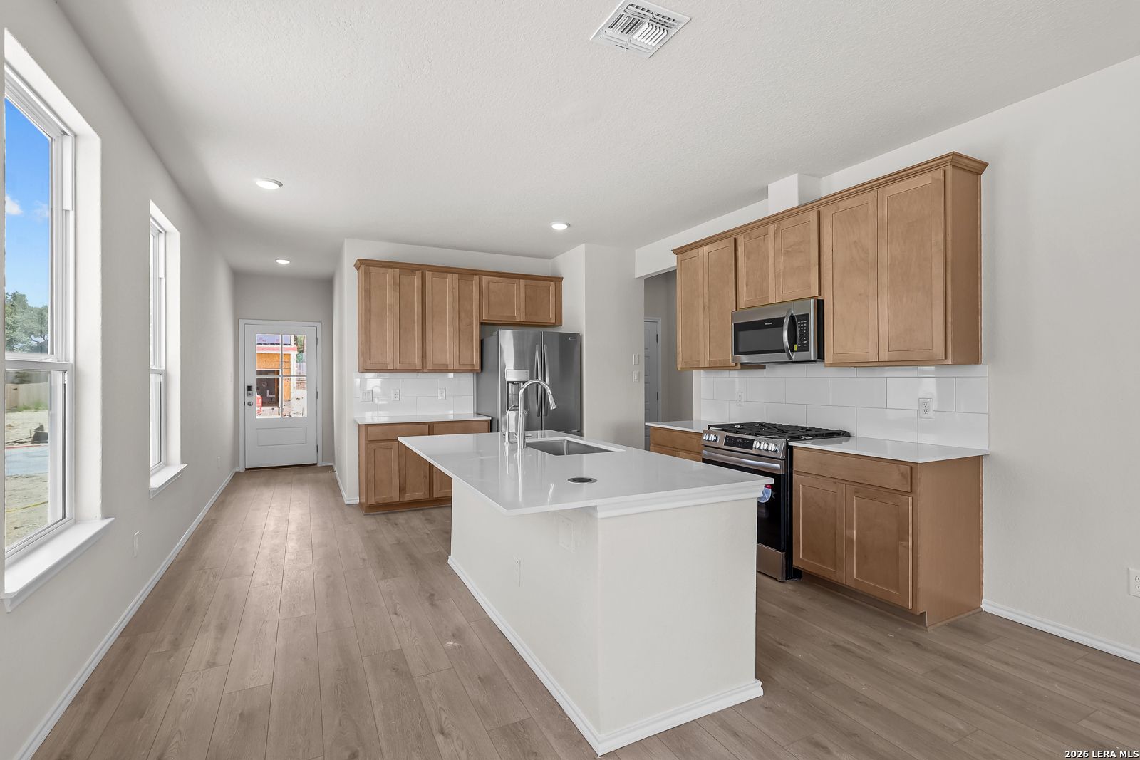 Modern kitchen with white quartz island, wood cabinets, and stainless appliances in Gillian B floor plan, San Antonio, TX.