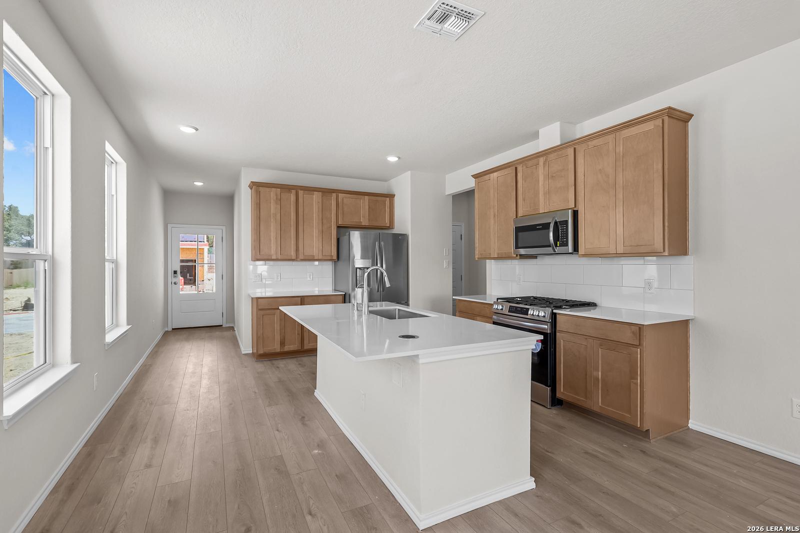Modern kitchen with white quartz island, wood cabinets, and stainless appliances in Gillian B floor plan, San Antonio, TX.