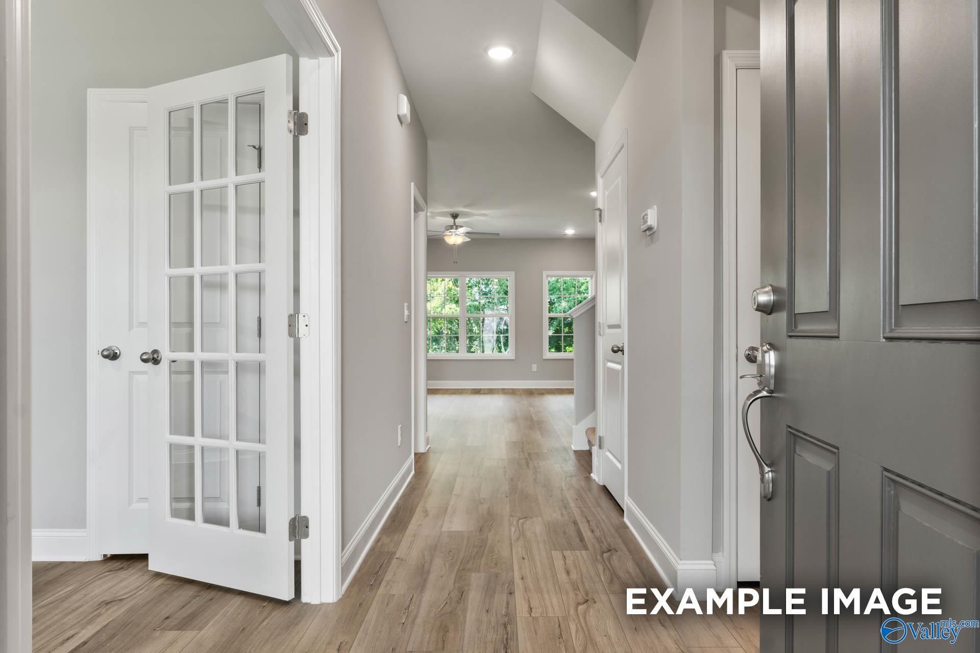 Bright hallway with hardwood floors, glass-paneled doors, and vaulted ceiling in Davidson Homes The Rockford D, Hazel Green, AL