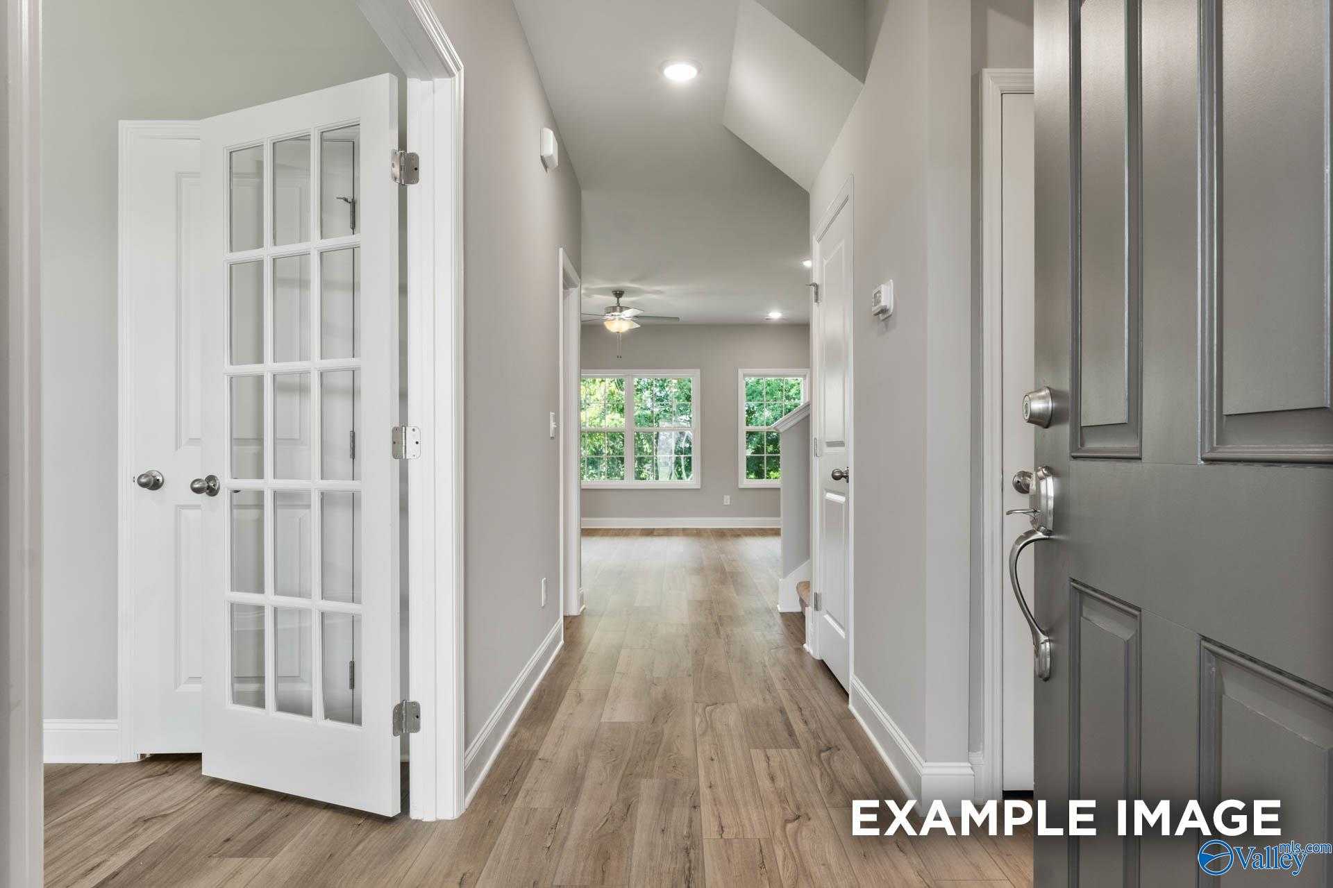 Bright hallway with hardwood floors, glass-paneled doors, and vaulted ceiling in Davidson Homes The Rockford D, Hazel Green, AL